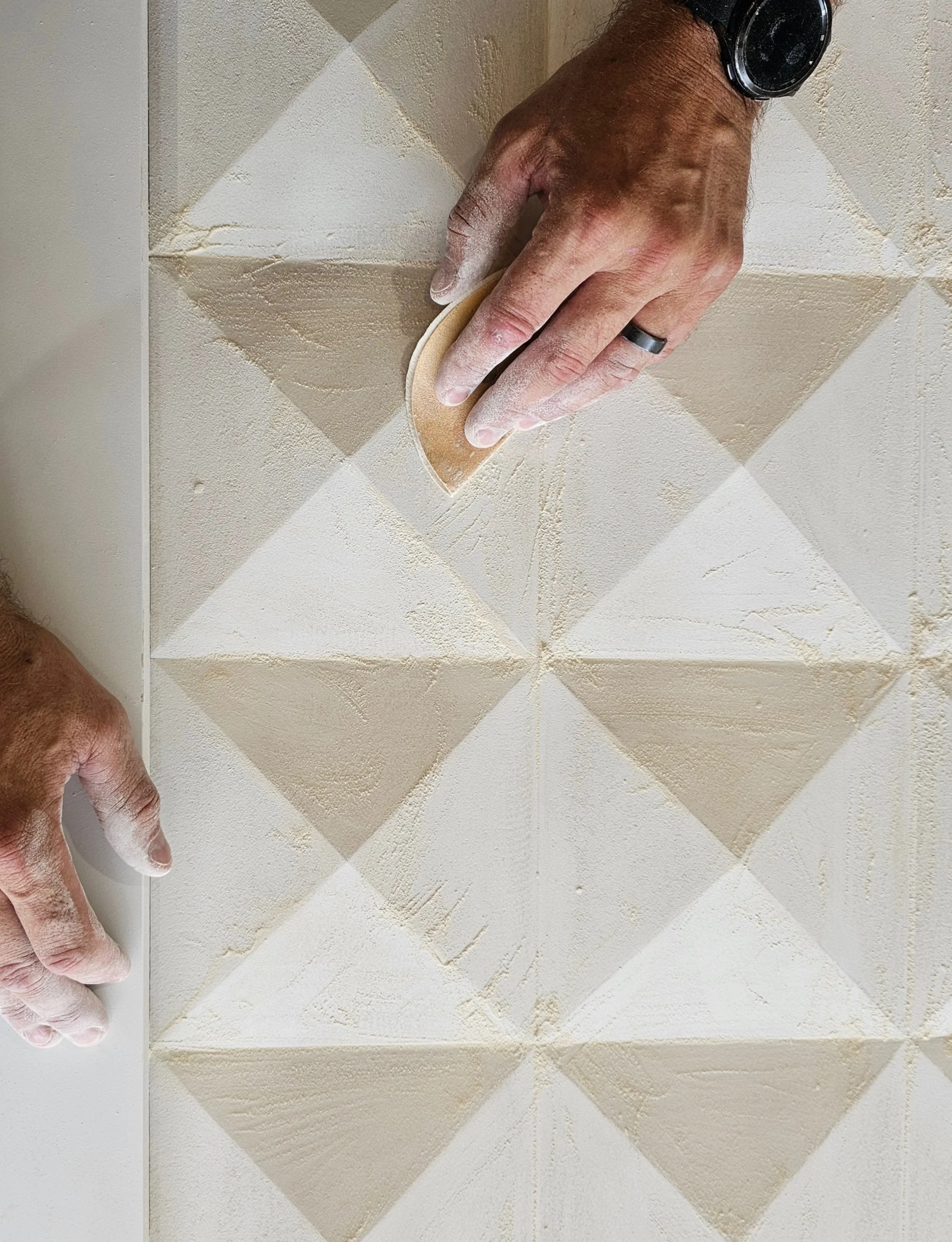 Person installing ceramic tiles on a floor using a trowel to spread adhesive.