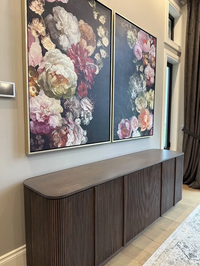 Two large floral paintings with dark backgrounds hanging above a wooden sideboard in a modern interior.