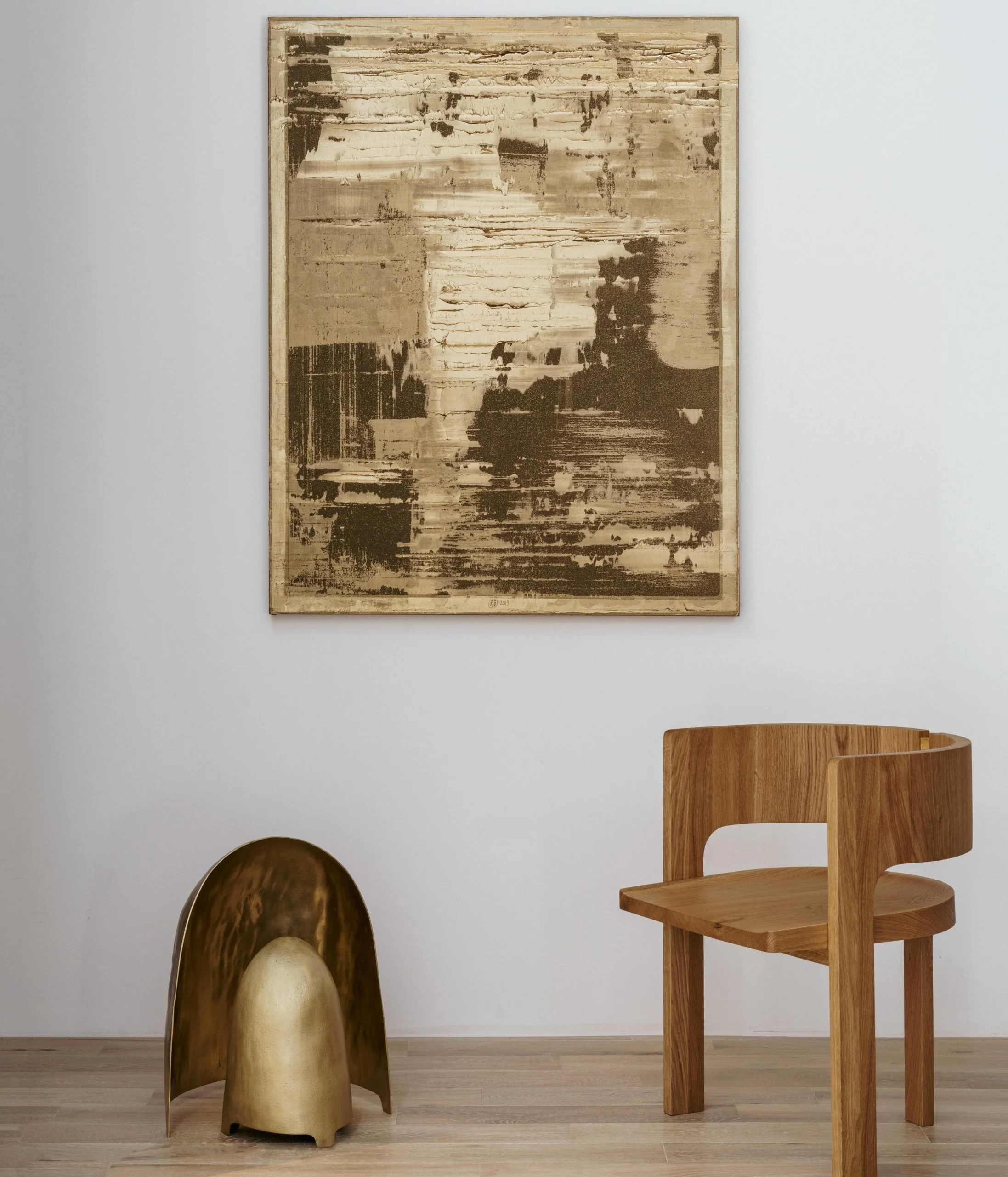 Minimalist interior with a large abstract painting on a white wall, a wooden chair, and a small brass sculpture.