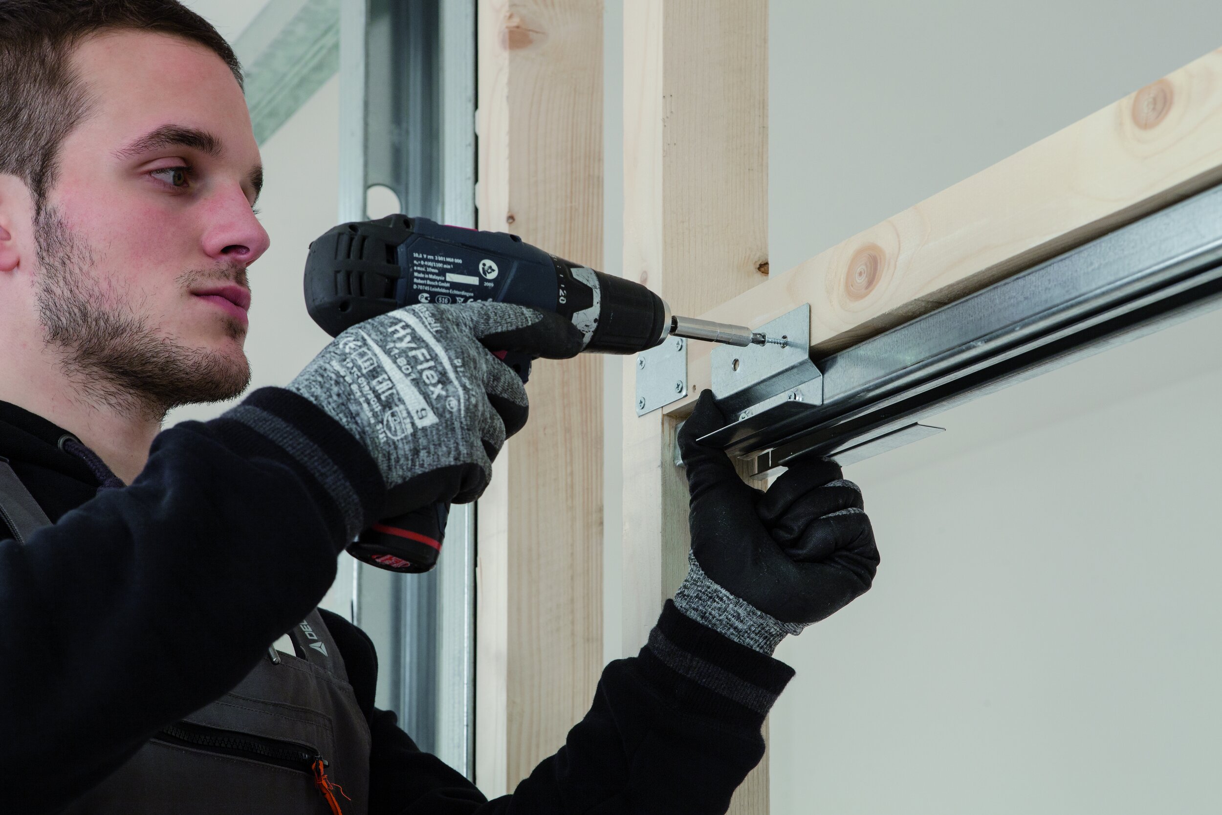 man drilling bracket onto stud work to install pocket door frame