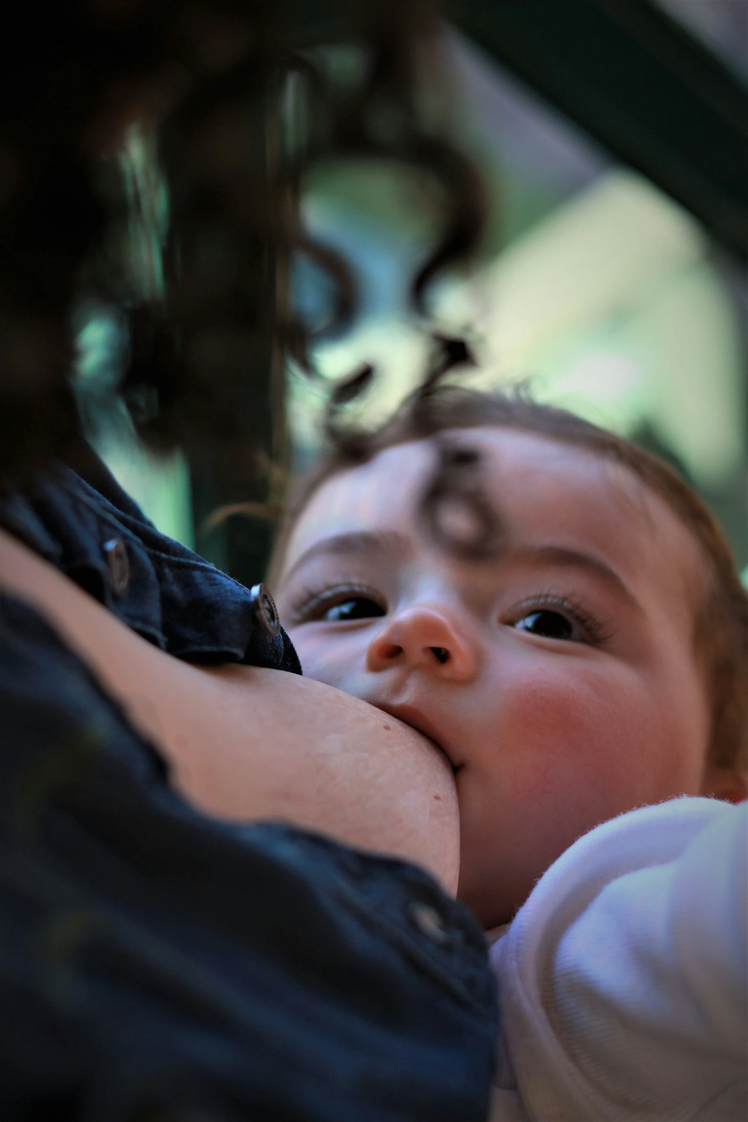 Eine Mutter stillt ihr Baby, während die beiden einander liebevoll und direkt in die Augen schauen.