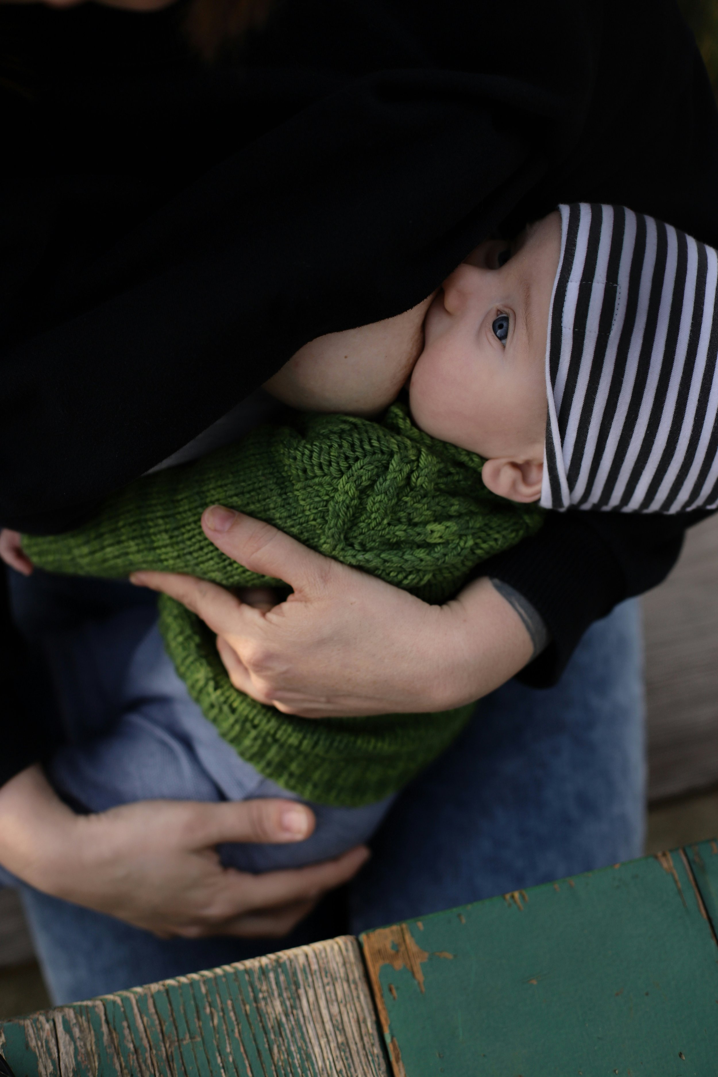 Eine junge Mutter stillt liebevoll ihr Baby, das eine gestreifte Mütze und eine grüne Strickjacke trägt.