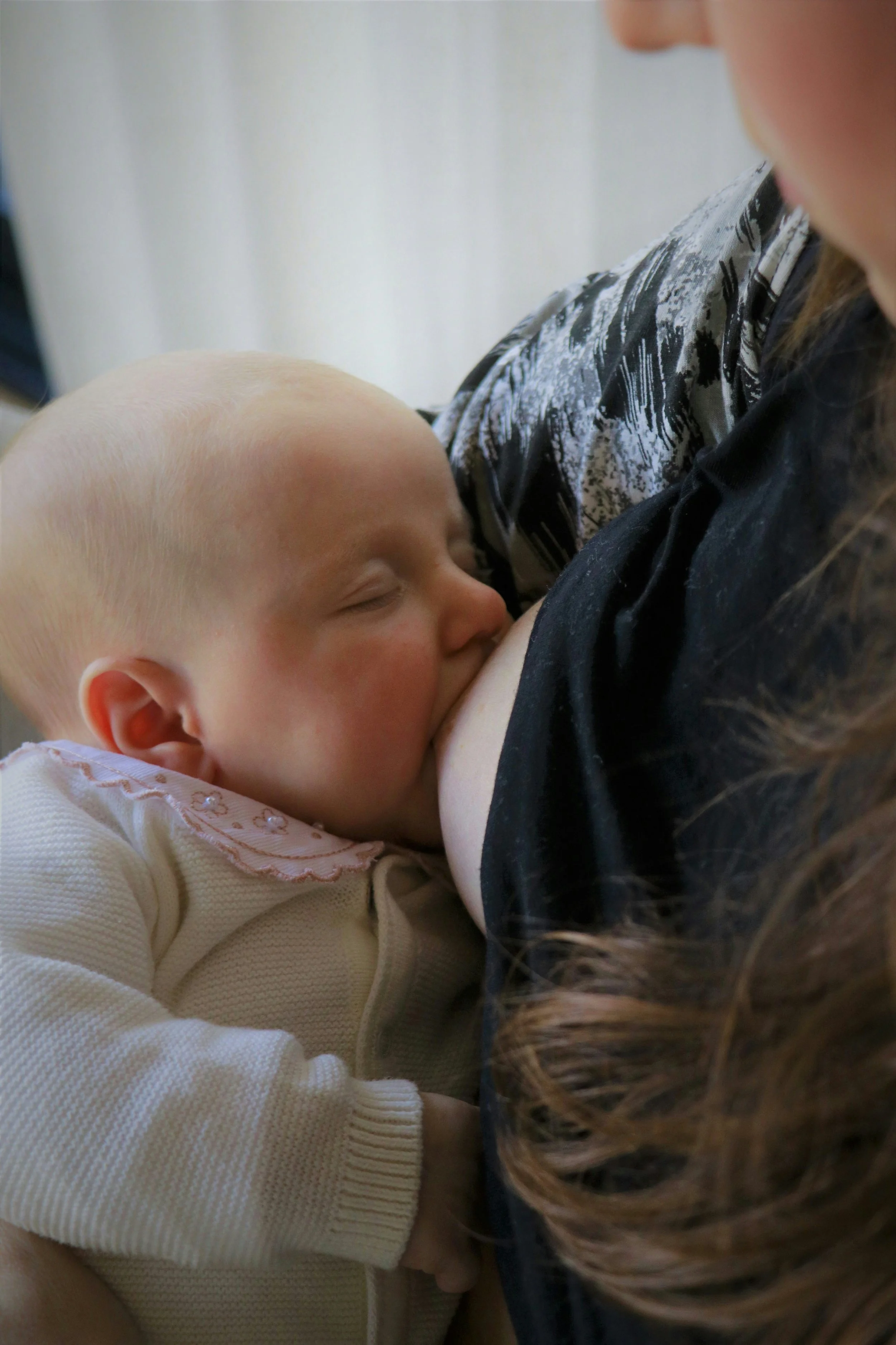 Ein schlafendes Baby liegt entspannt im Arm der Mutter, nachdem es beim Stillen eingeschlafen ist.