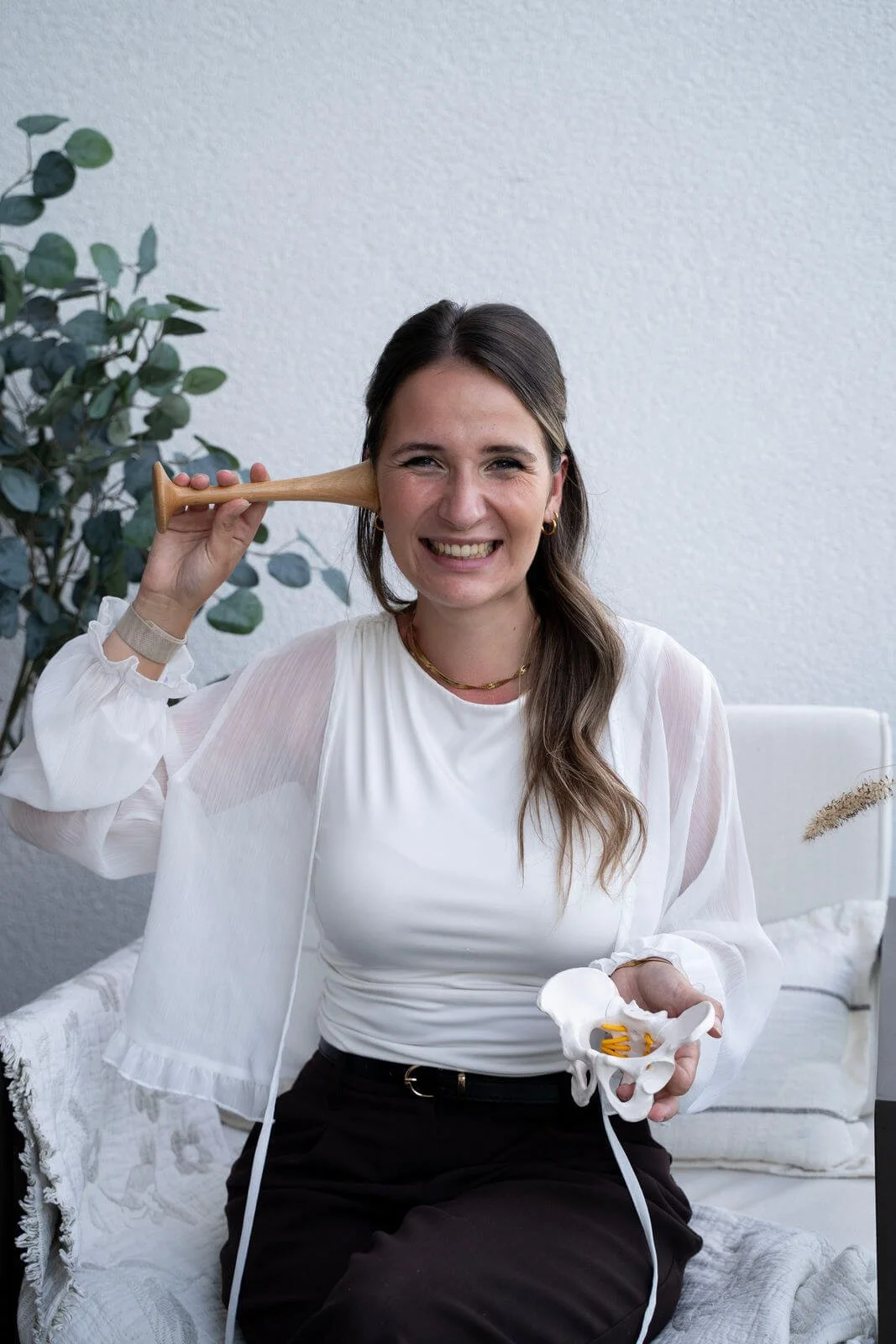 Hebamme Sina mit Hörrohr und Beckenmodel in der Hand