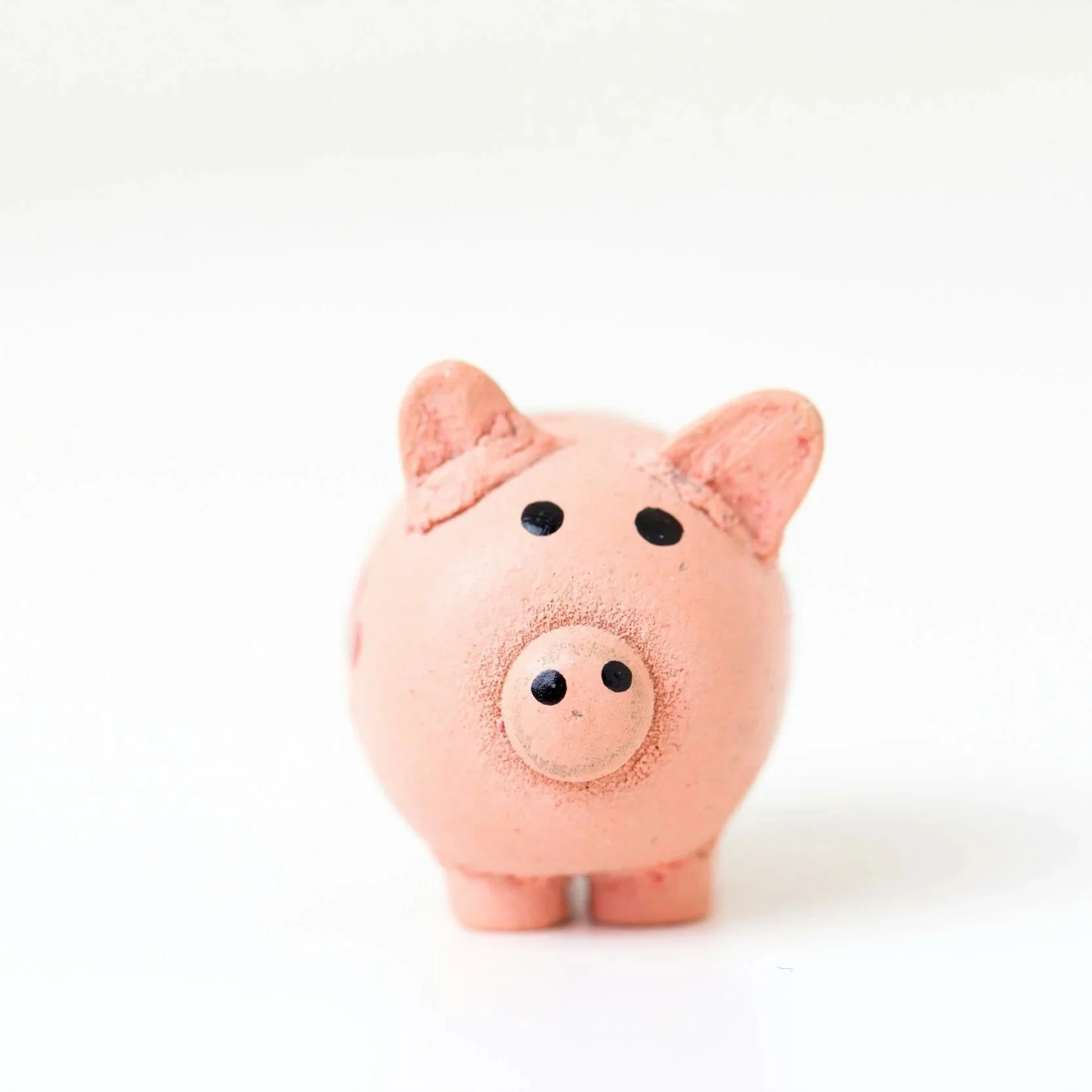 Pink ceramic piggy bank with black eyes and a snout, on a white background.