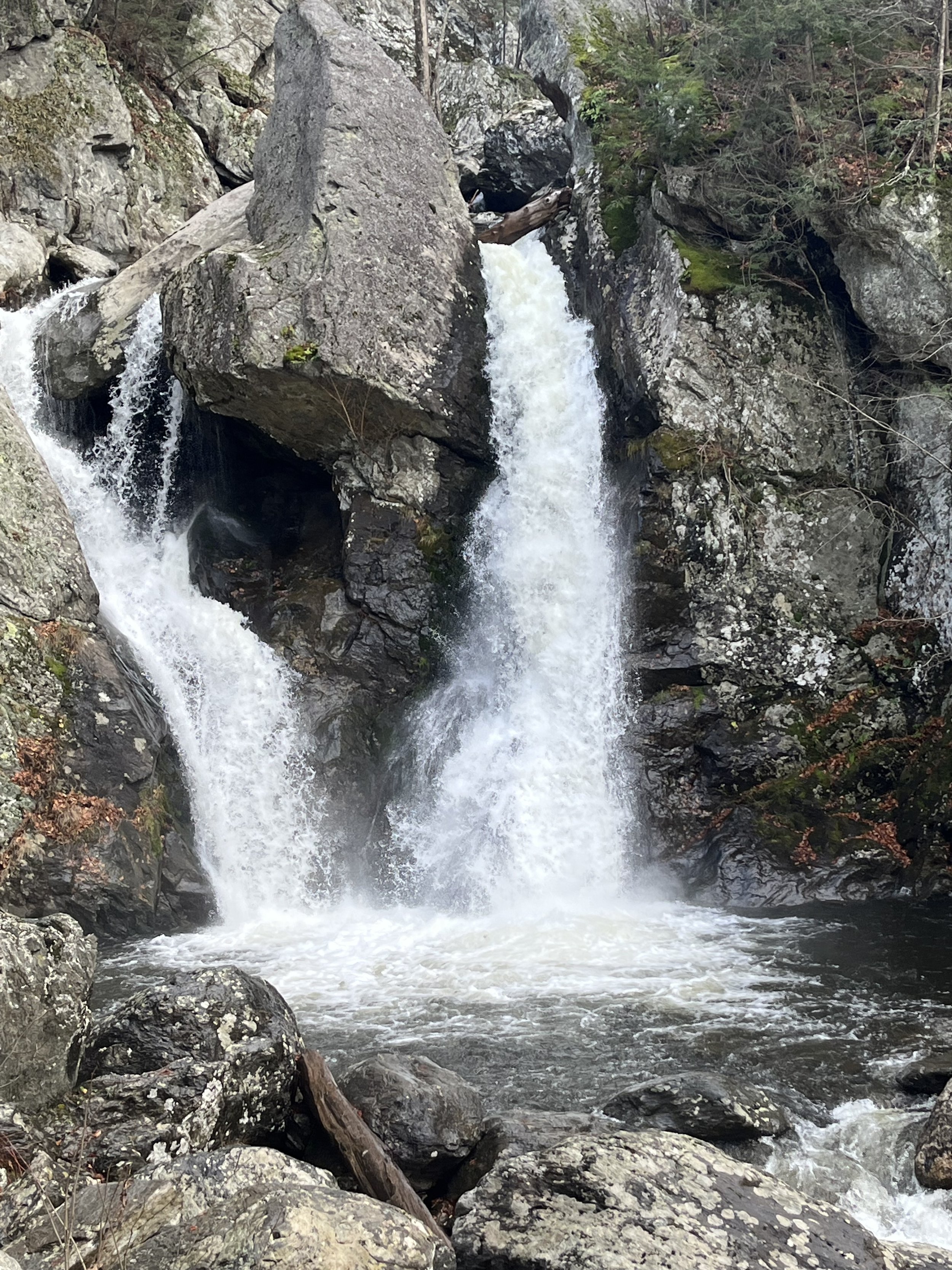 Waterfall cascading over large rocks in a wooded area.