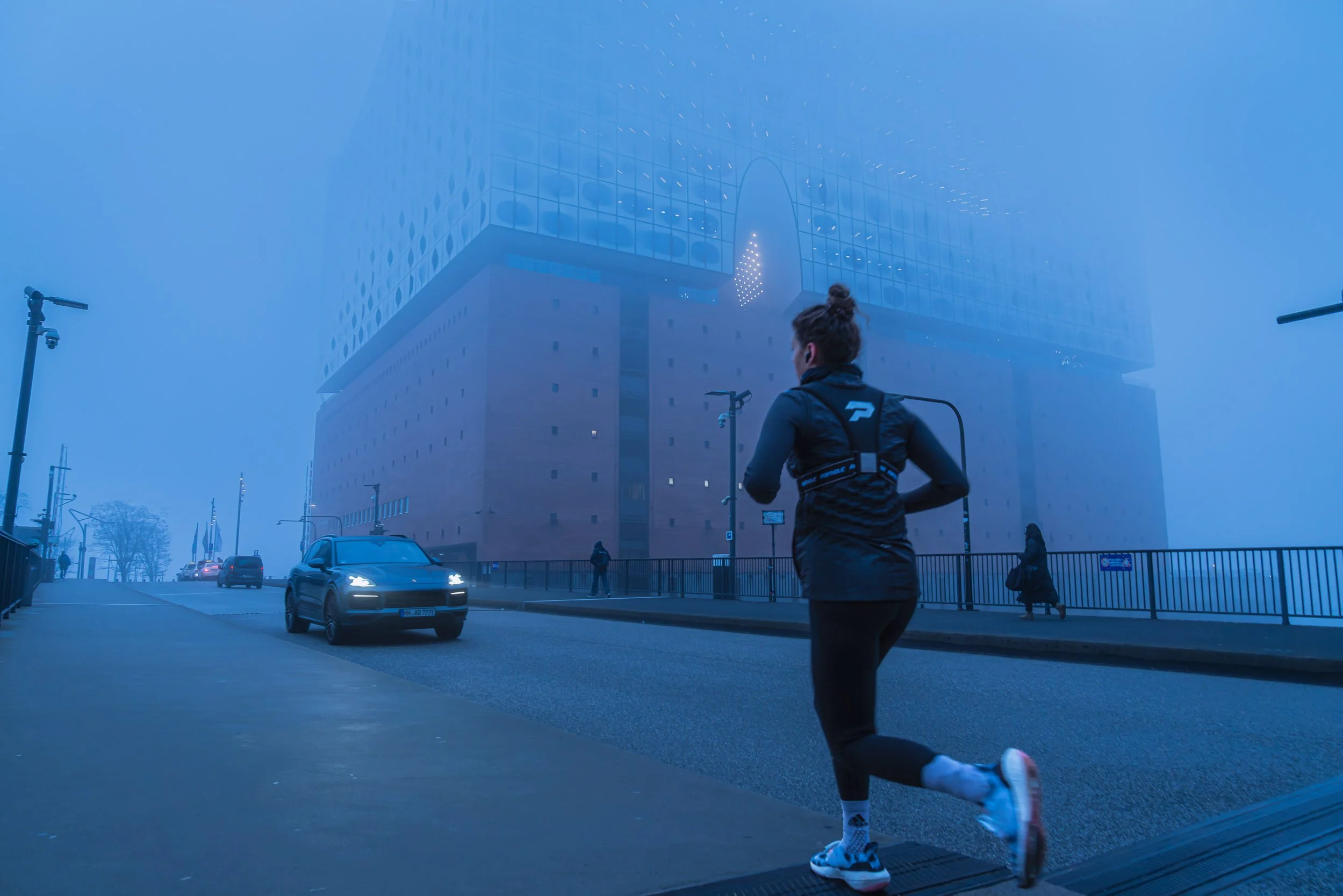 A woman running on a city street in foggy weather with tall modern buildings and cars passing by.