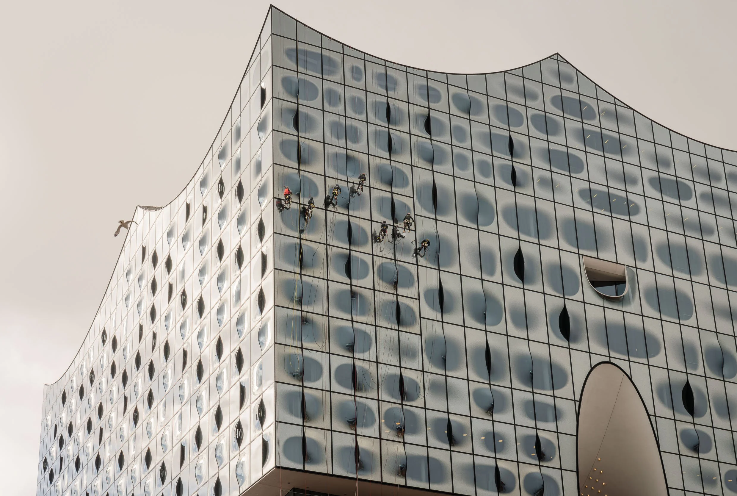 Workers cleaning the glass facade of a modern commercial building with rounded and patterned windows.