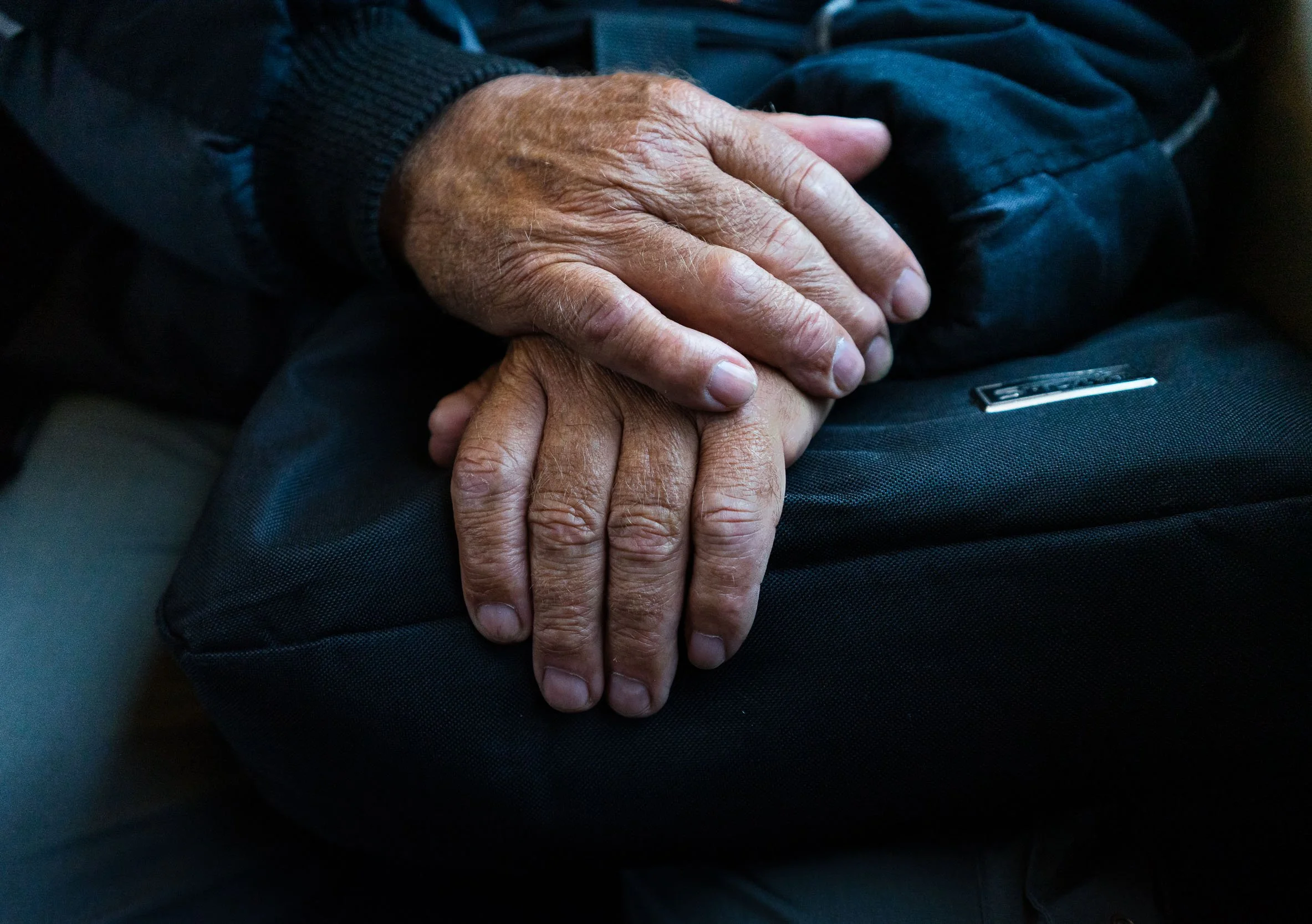 Close-up of two elderly hands gently resting on top of each other, placed on a black bag.