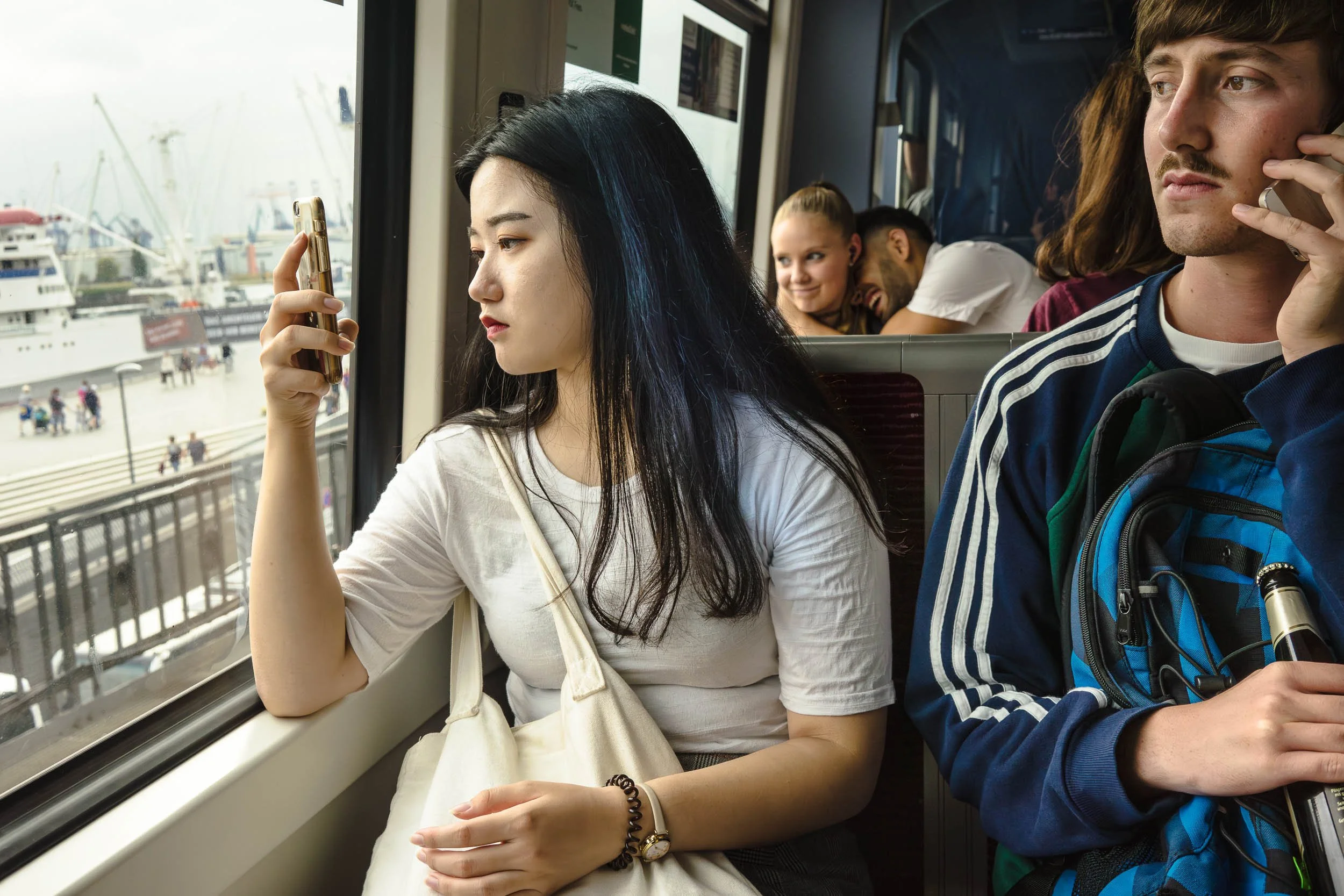 A group of young people on a ferry, with a woman looking at her phone, a man on the phone, and two people in the background smiling.