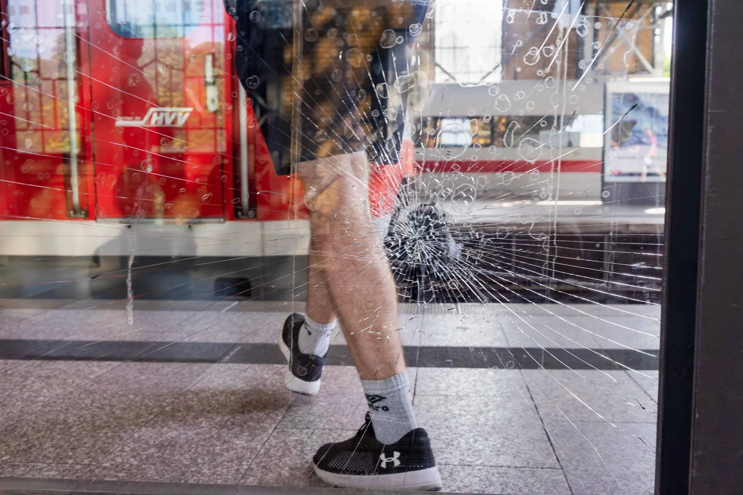 A person walking through a glass door that has a large circular hole shattered in it, with spider web cracks radiating from the center of the damage.