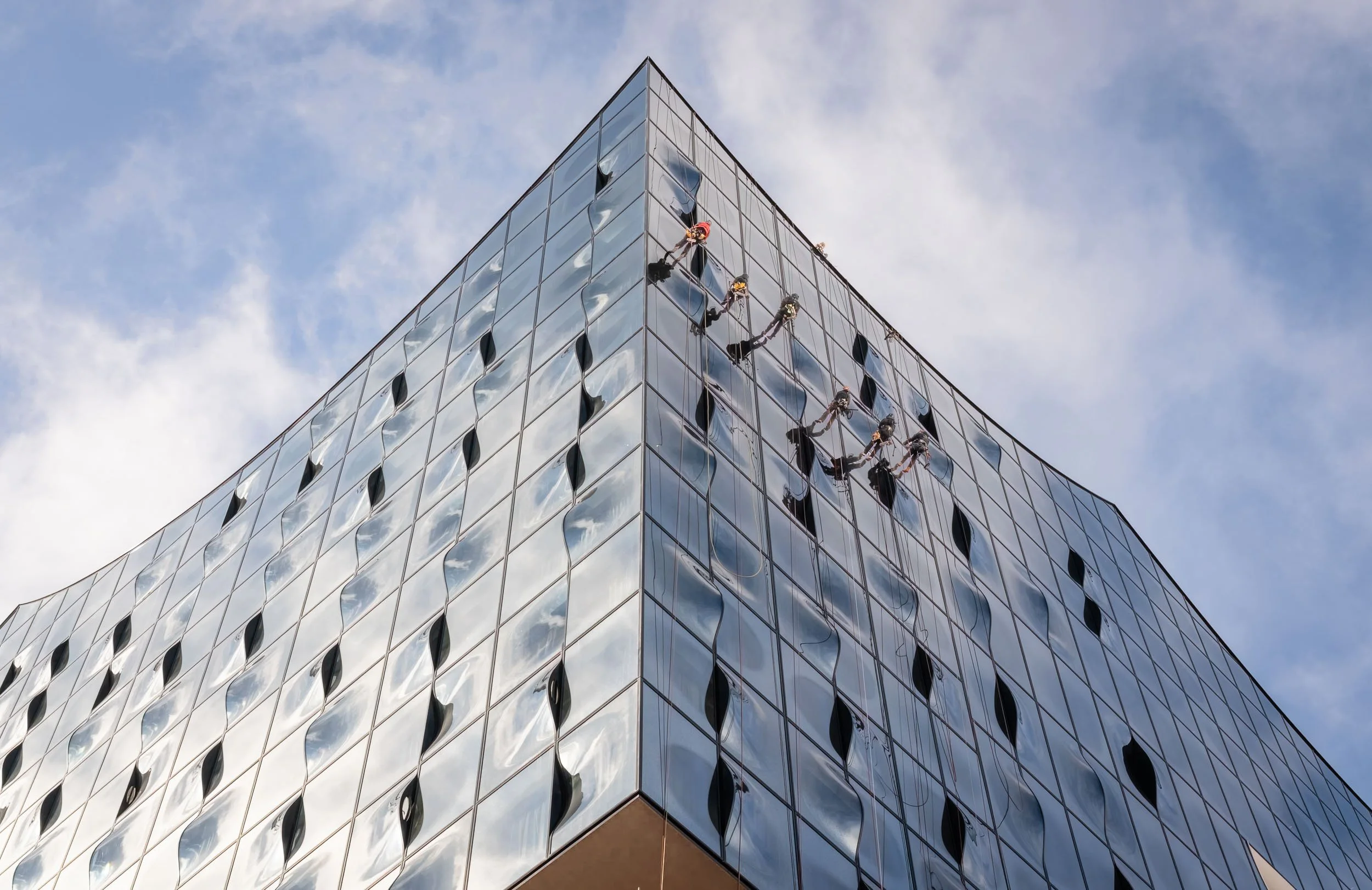 Window washers cleaning the exterior glass of a modern office building with reflective windows, high above the ground, during daytime.