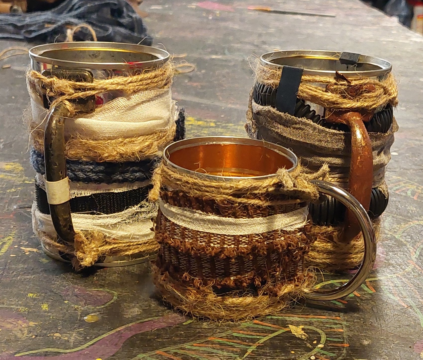 Wine cups made of recycled/scrap materials. Started with aluminum can bases, then added strips of fabric, hose, gauze, velcro, twine, etc. Finished by securely tying on various handle shaped hardware.