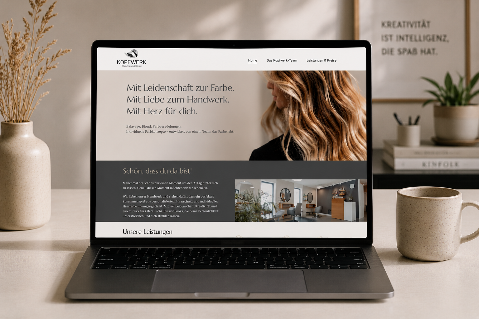 Laptop zeigt Webseite von Friseursalon mit Begriffen wie Leidenschaft für Farbe und Handwerk, Frauen mit lockigem Haar im Hintergrund, zwei Tassen, einer Vase mit Trockenblumen, eine Pflanze und Bücher im Raum.