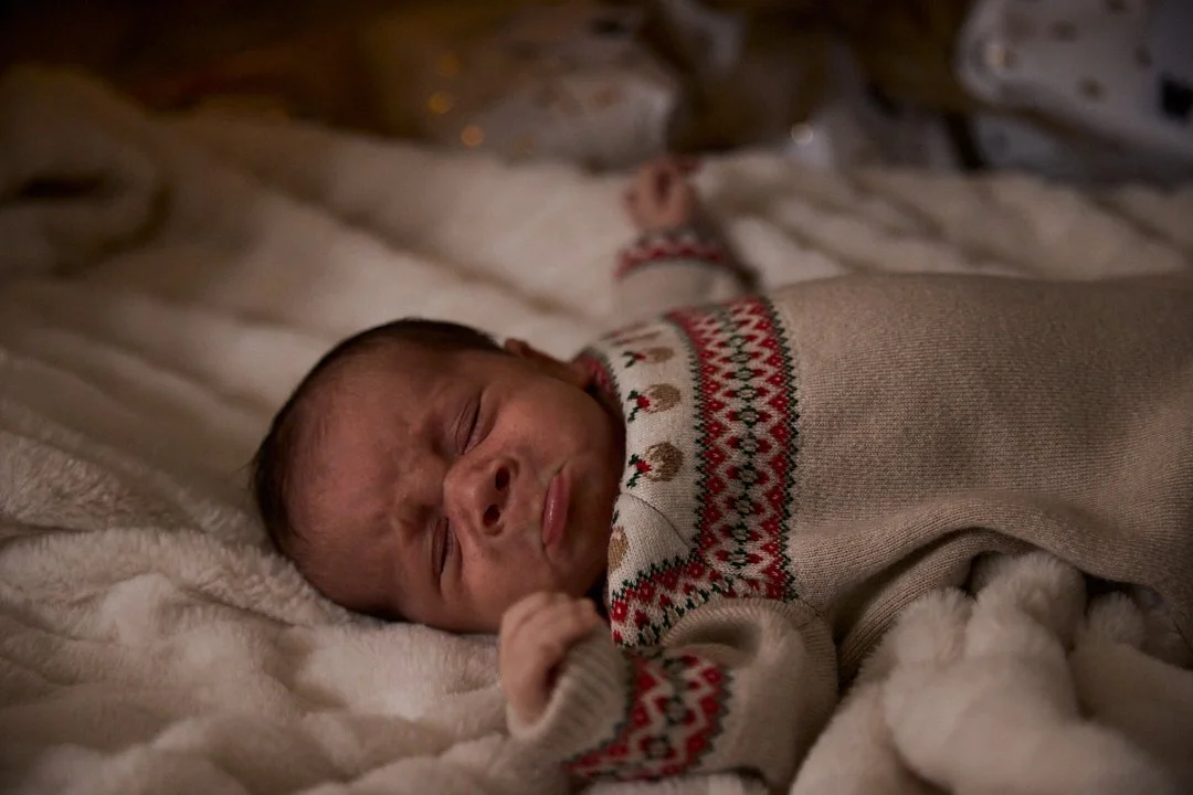 A newborn baby sleeping peacefully on a soft blanket, wearing a festive sweater with a red and green pattern.