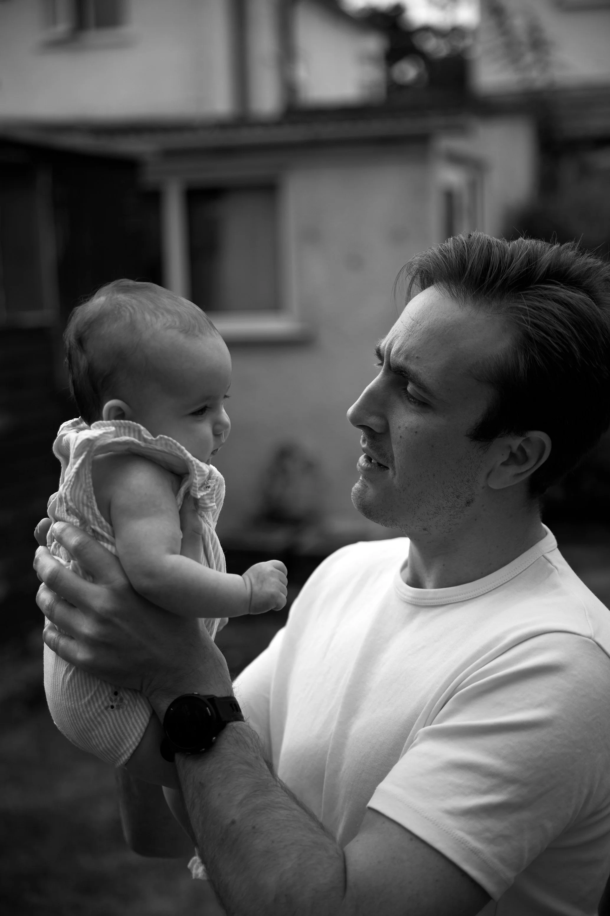 A man holding a baby girl and looking at her with a tender expression outdoors in black and white.