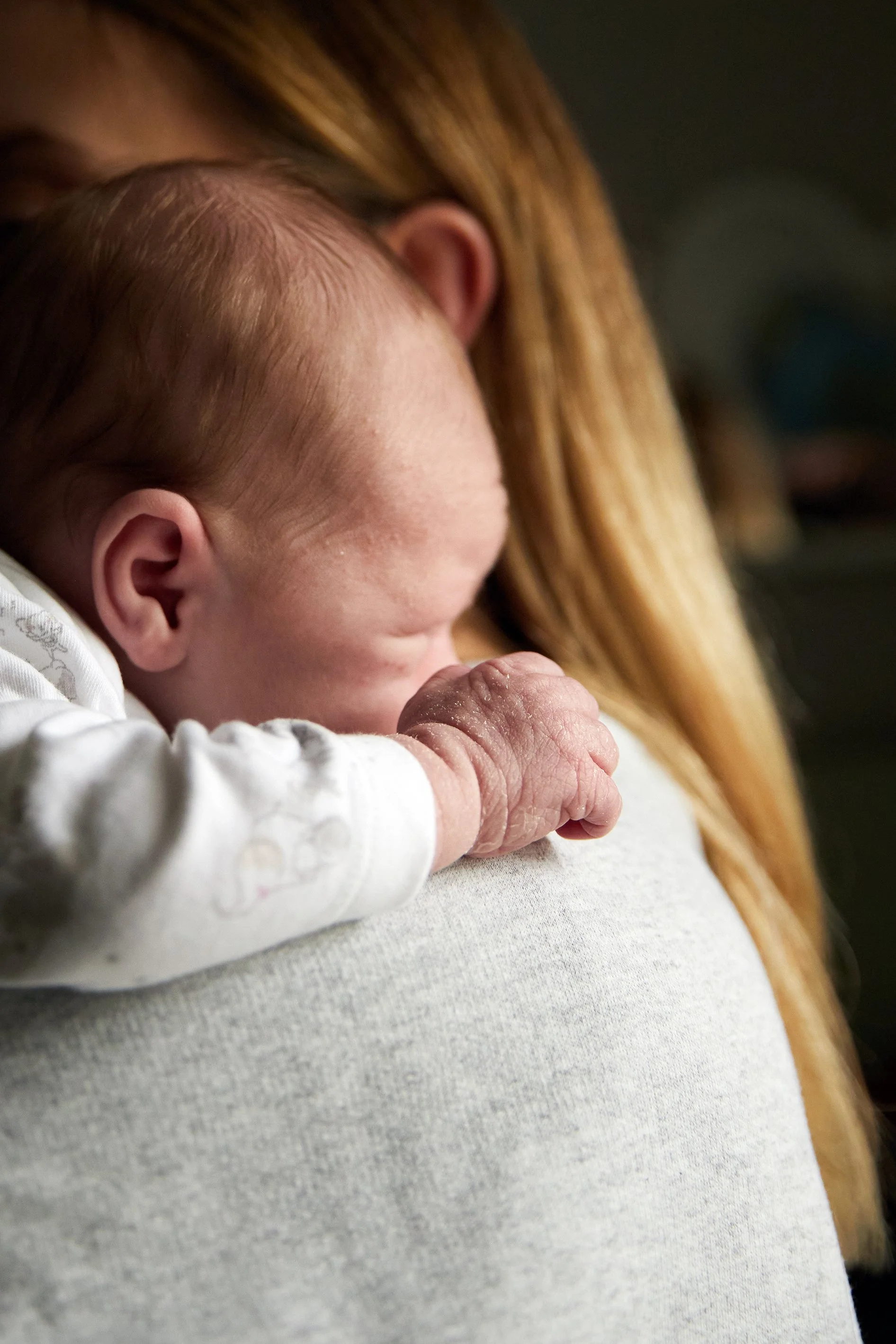 A newborn baby with red hair resting on an adult's shoulder, seen in close-up profile shot.