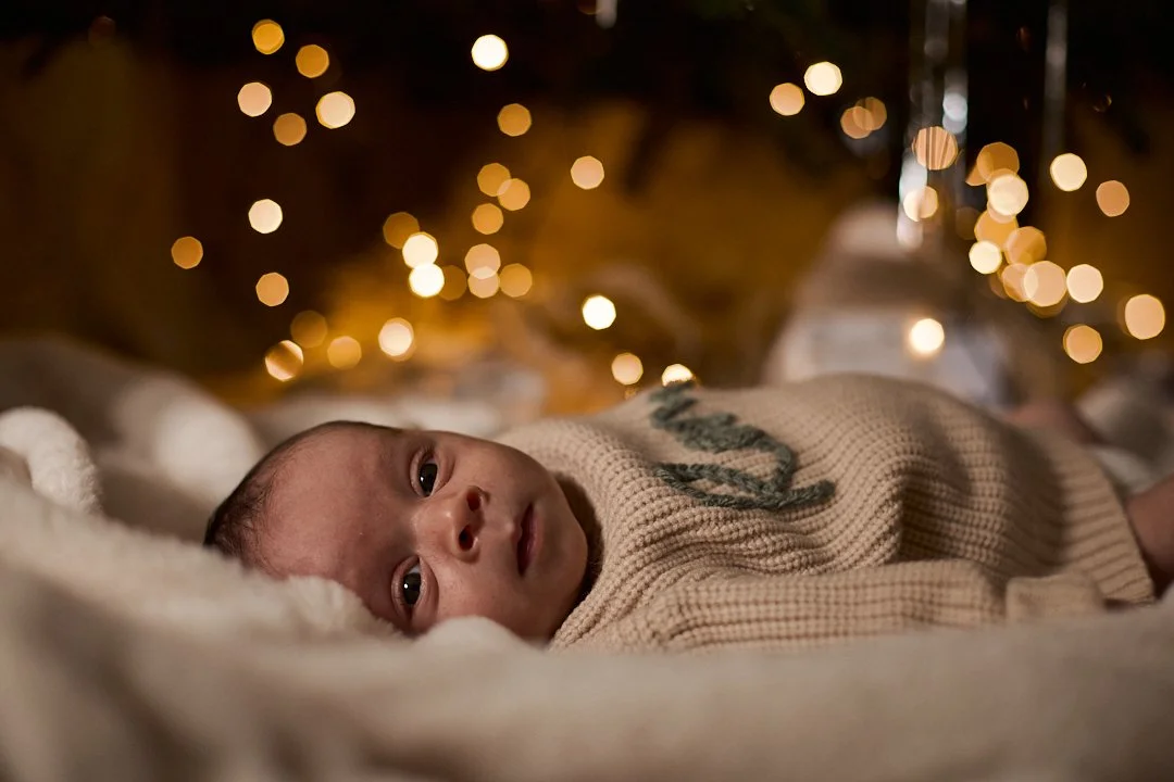 Baby lying on a soft blanket with blurred Christmas lights in the background.