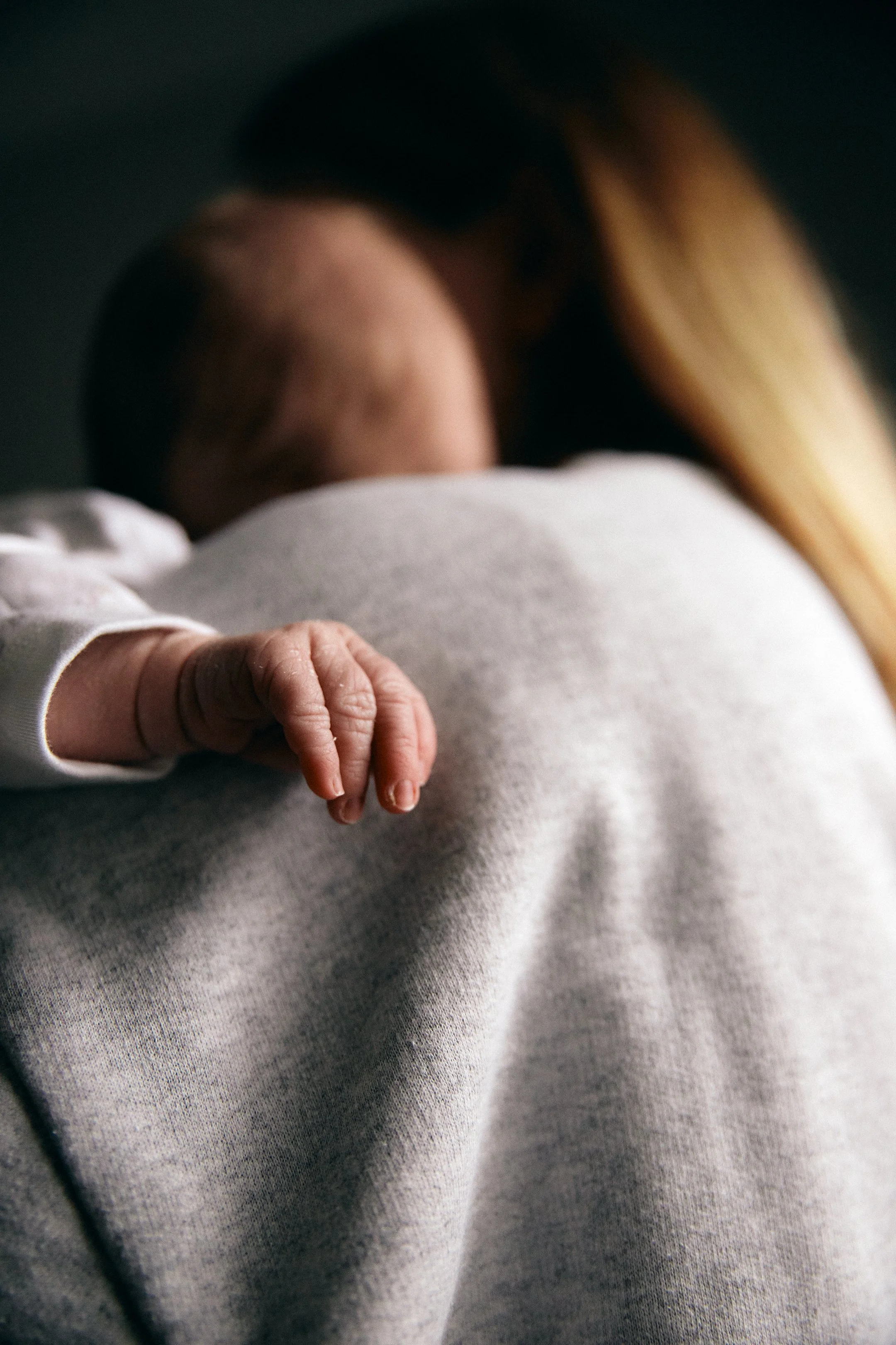 Close-up of a baby's hand resting on an adult's shoulder, with the adult's back and long hair visible in the background.