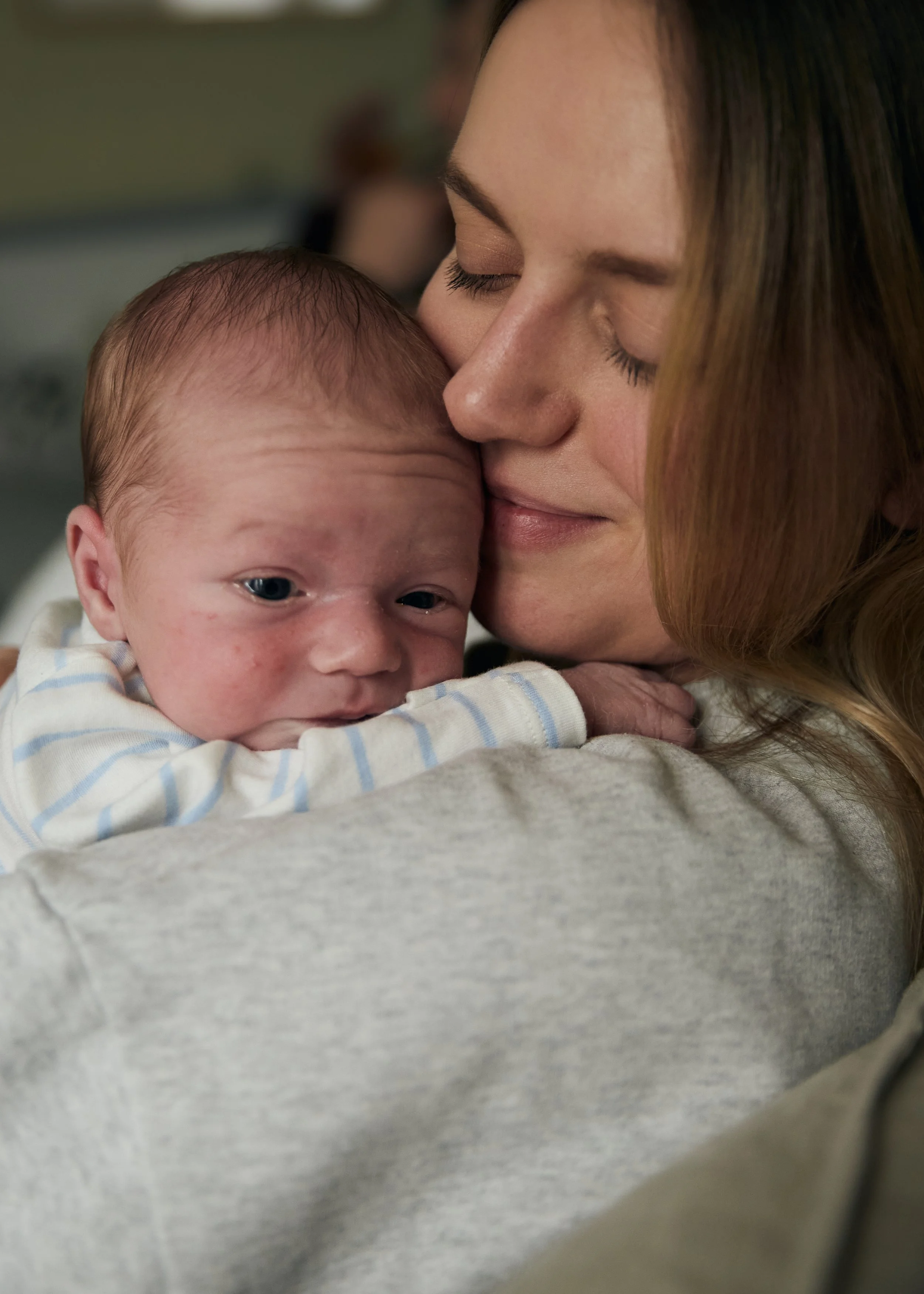 A woman holding a newborn baby close to her face, with both eyes closed, in an affectionate moment.
