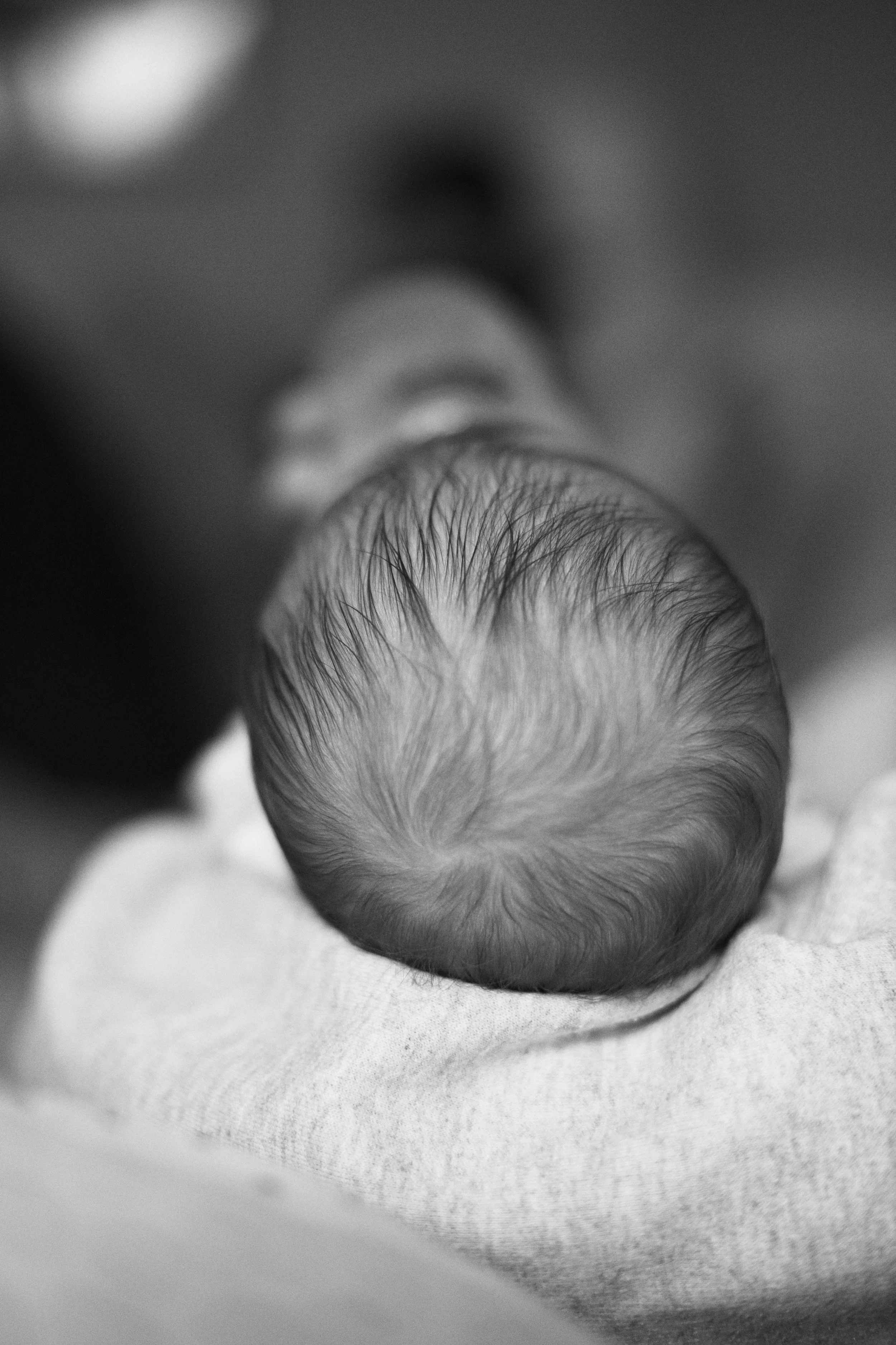 Black and white photo of a baby with wet hair, resting their head on a soft surface.