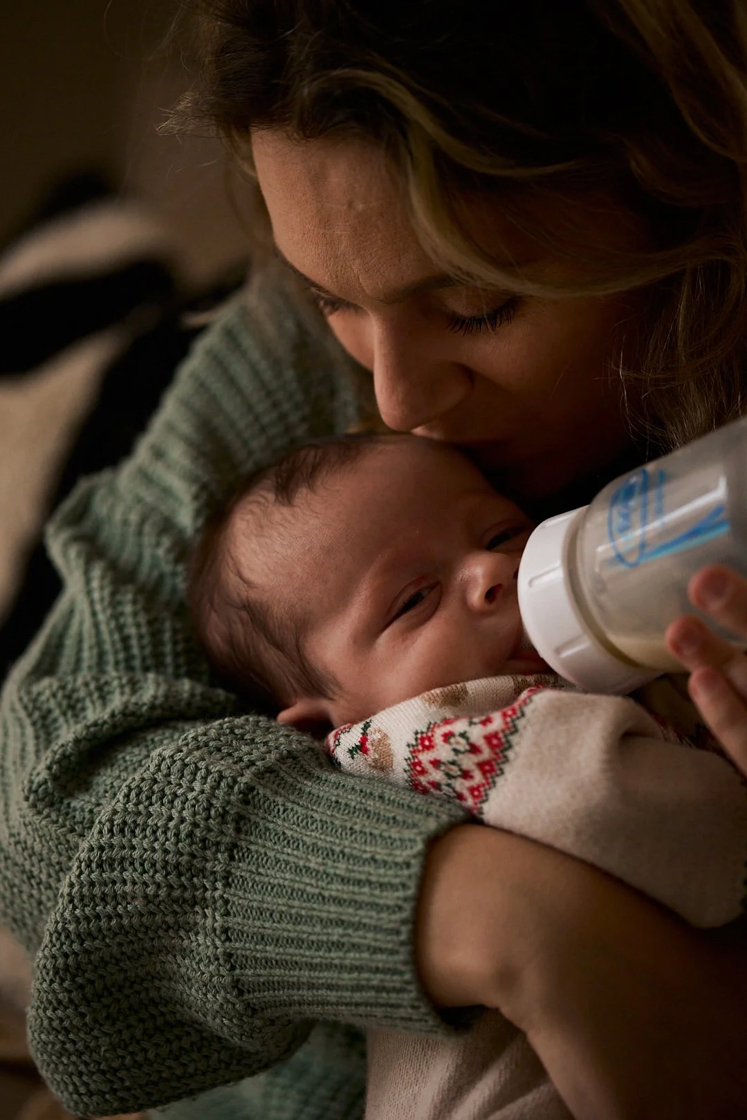 A woman holding a baby while feeding them with a bottle.