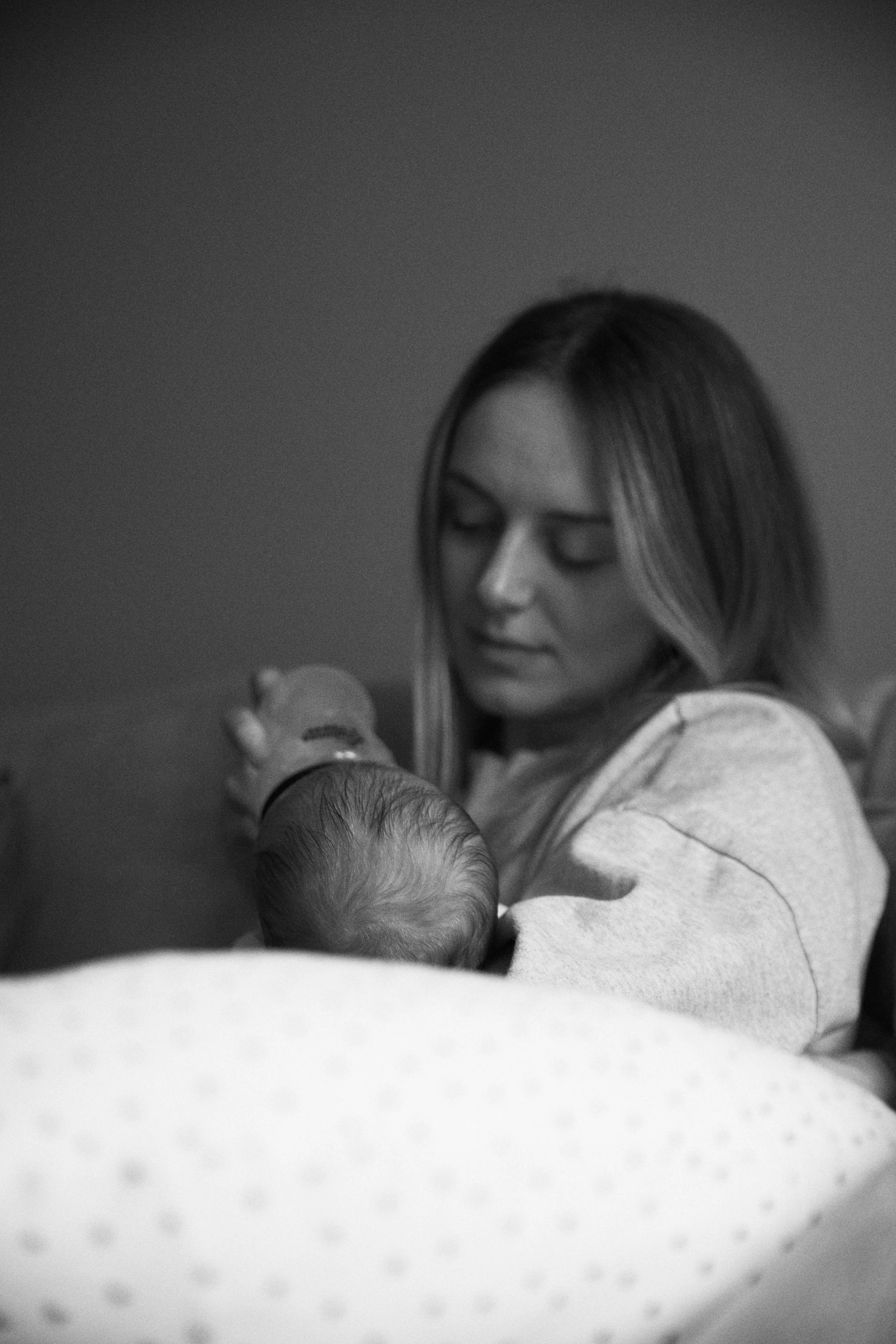 A woman with long hair looking down while bottle-feeding a newborn baby lying in a crib.