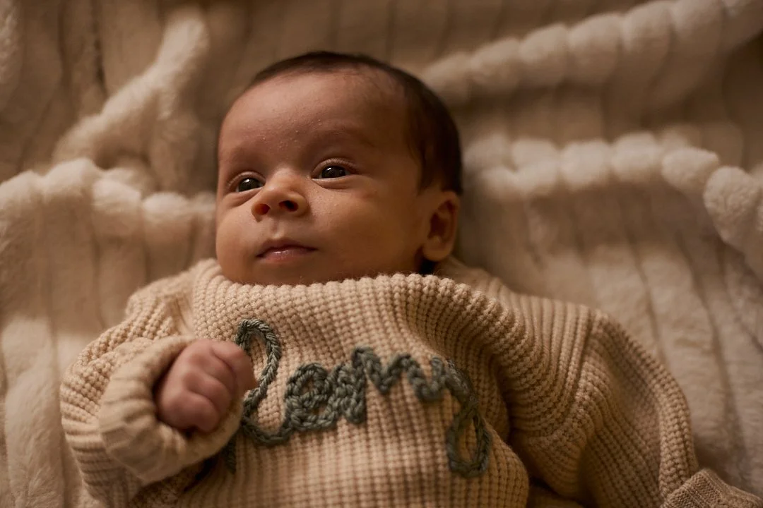 Close-up of a baby lying on a soft blanket, wearing a cream-colored sweater with the word 'love' embroidered on it.