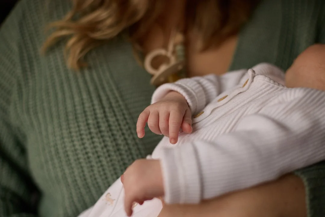 A woman holding a baby close to her chest, with the baby's hand resting on the woman's arm.