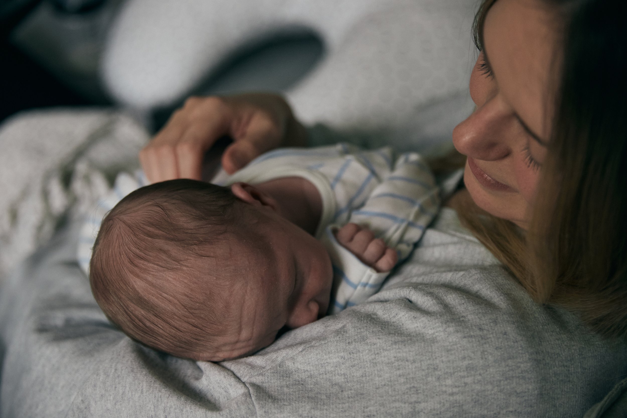 A woman holding and smiling at a newborn baby lying on her chest.