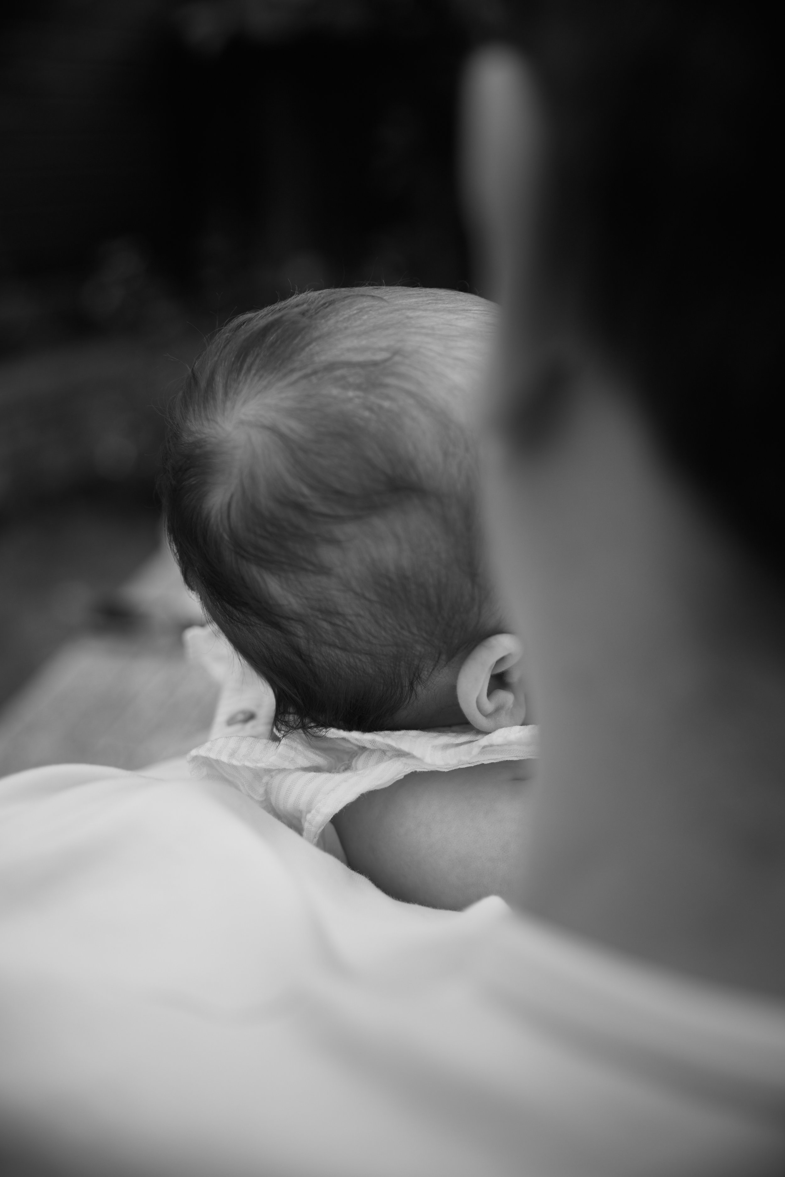 Close-up of a baby's head resting on an adult's shoulder, with the focus on the baby's hair and ear, in black and white