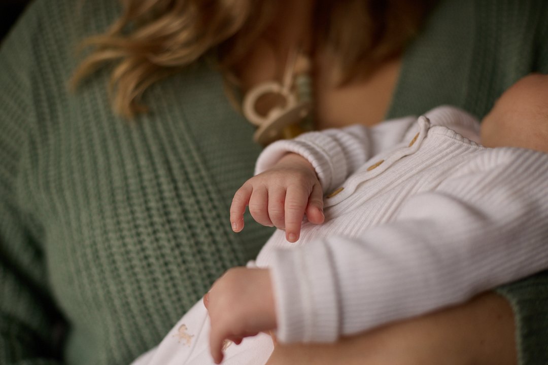 Close-up of a woman holding a baby, focusing on the baby's hand and partial view of the baby's body.