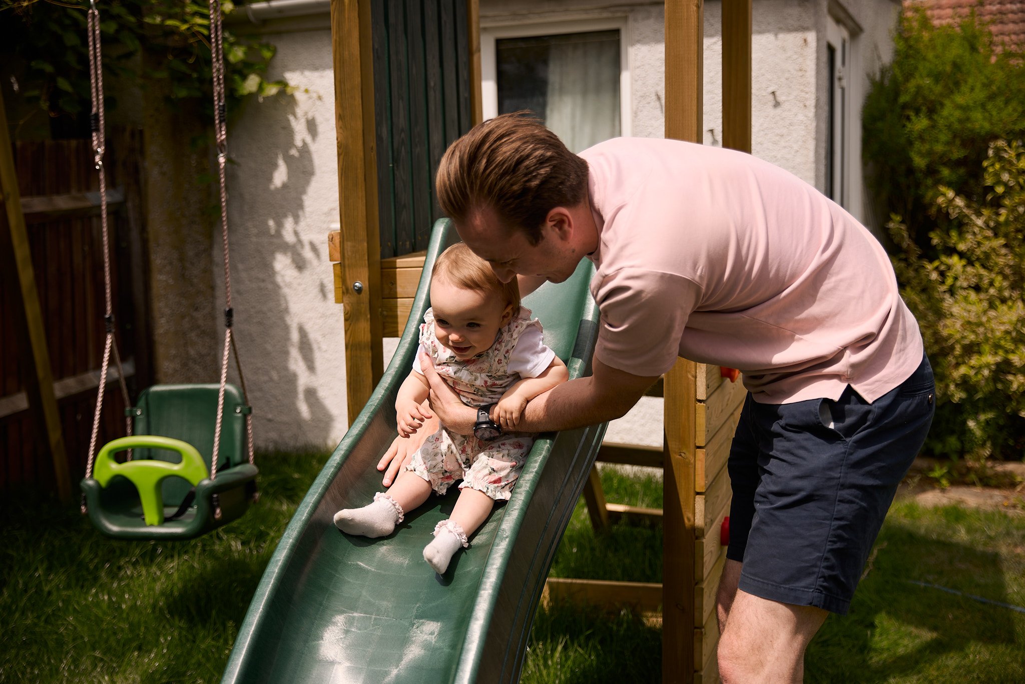 Man helping young girl go down outdoor slide in backyard