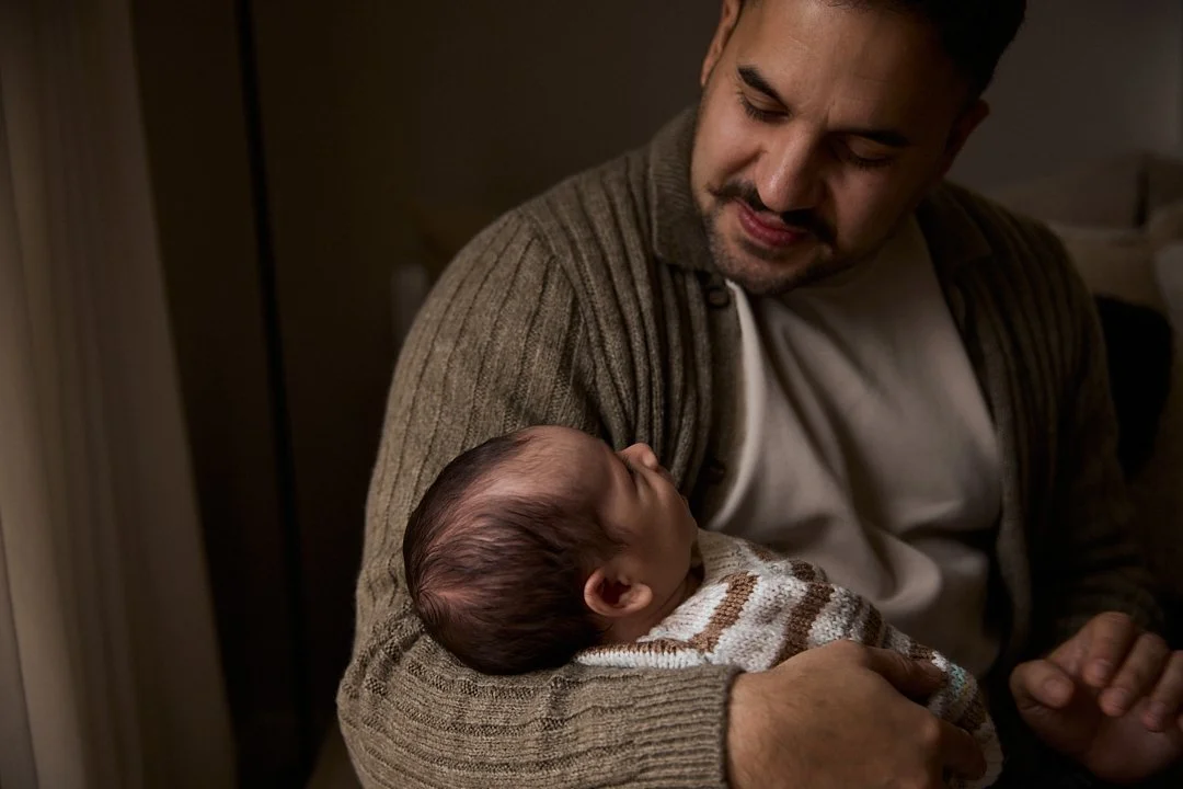 A man holds a newborn baby in his arms, looking down at the infant with affection.