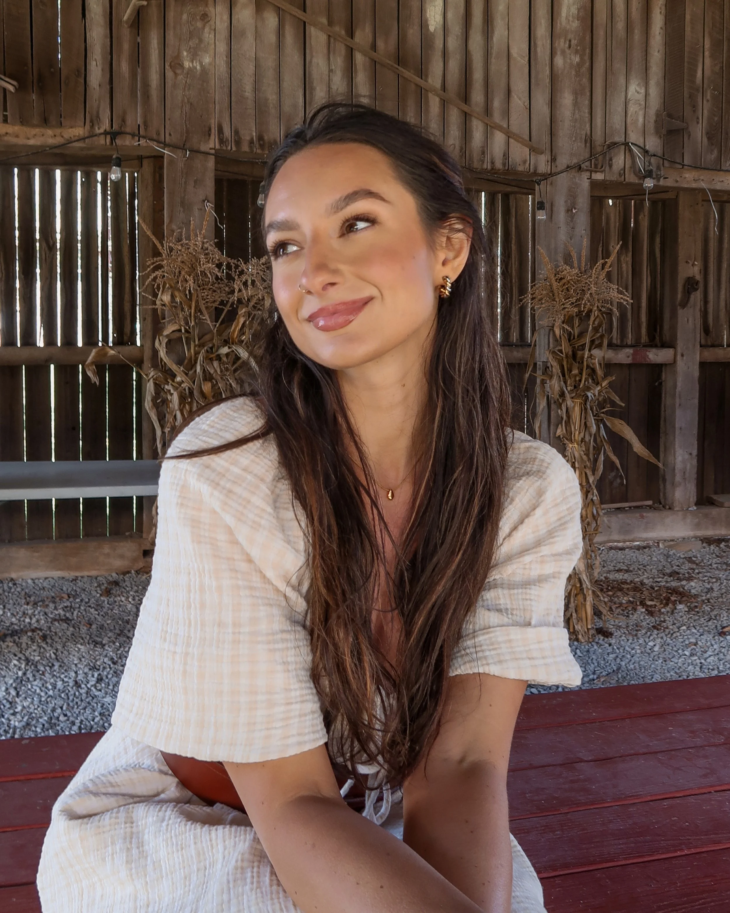 Meg Nailling with long dark hair and gold earrings wearing a cream dress while sitting outdoors at a farm in Northern Virginia.