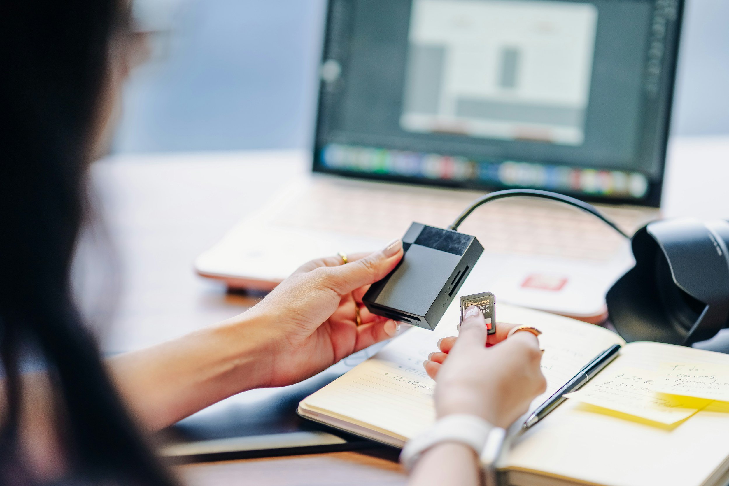 Person connecting a microSD card to a device at a desk with a laptop, notebook, pen, and monitoring equipment.