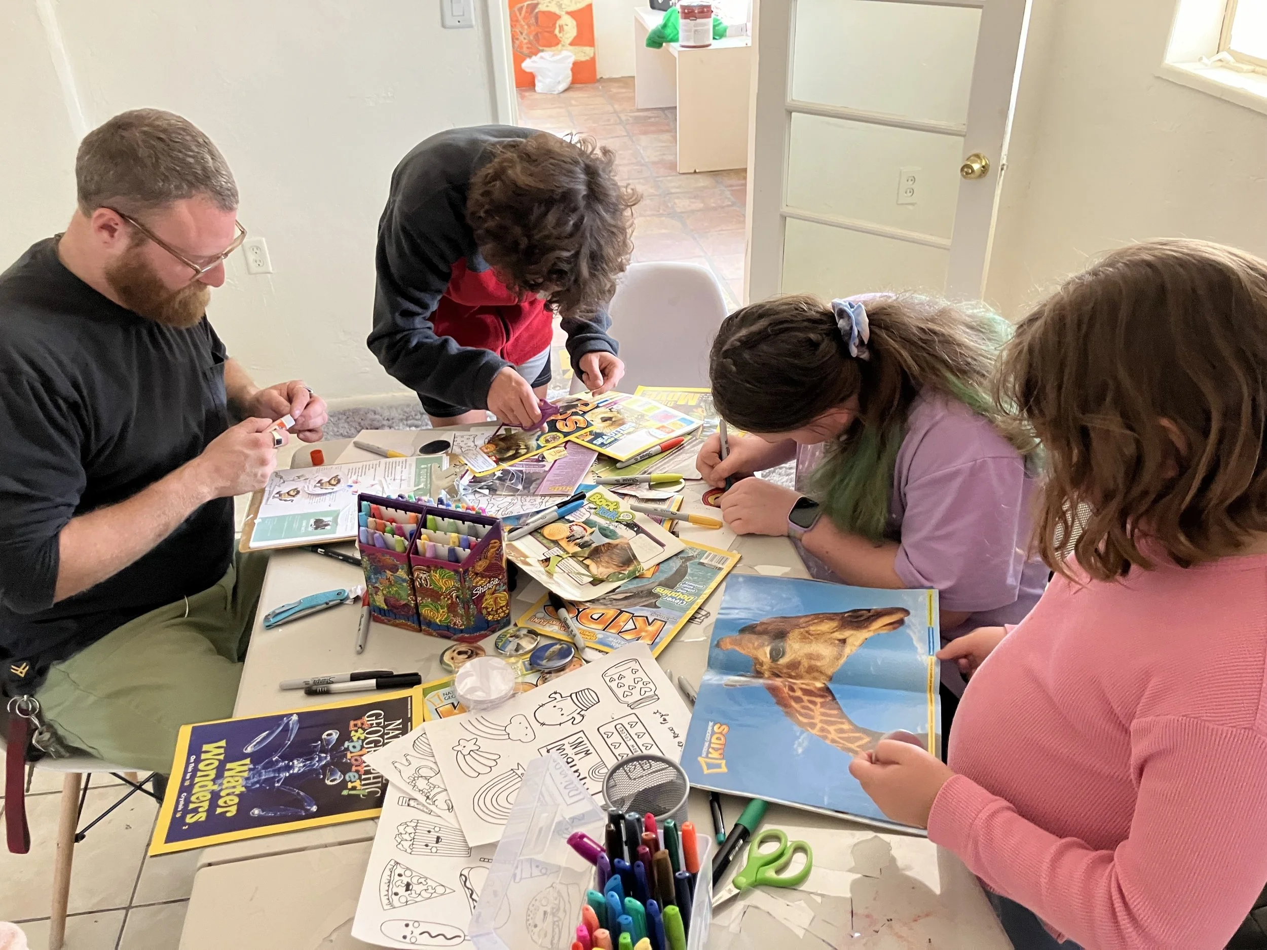 3 students and 1 staff member sit around a table cutting out magazine images to make buttons
