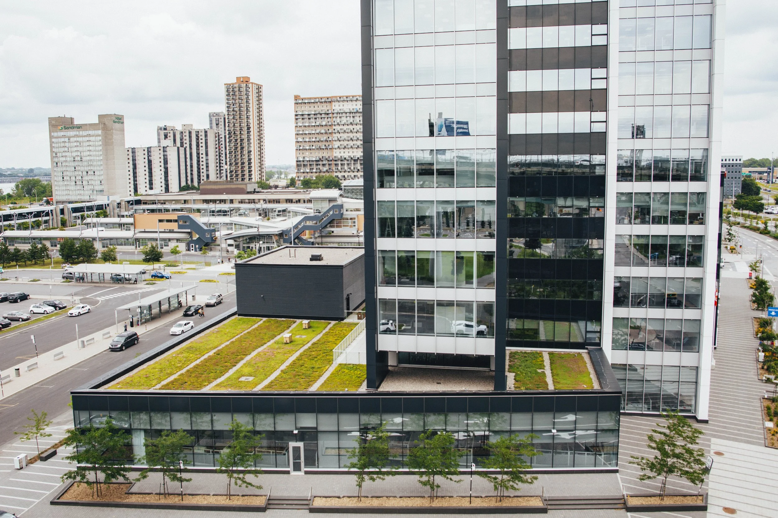 Vue aérienne d'un bâtiment moderne avec une façade en verre, un toit végétalisé et un parking environnant.