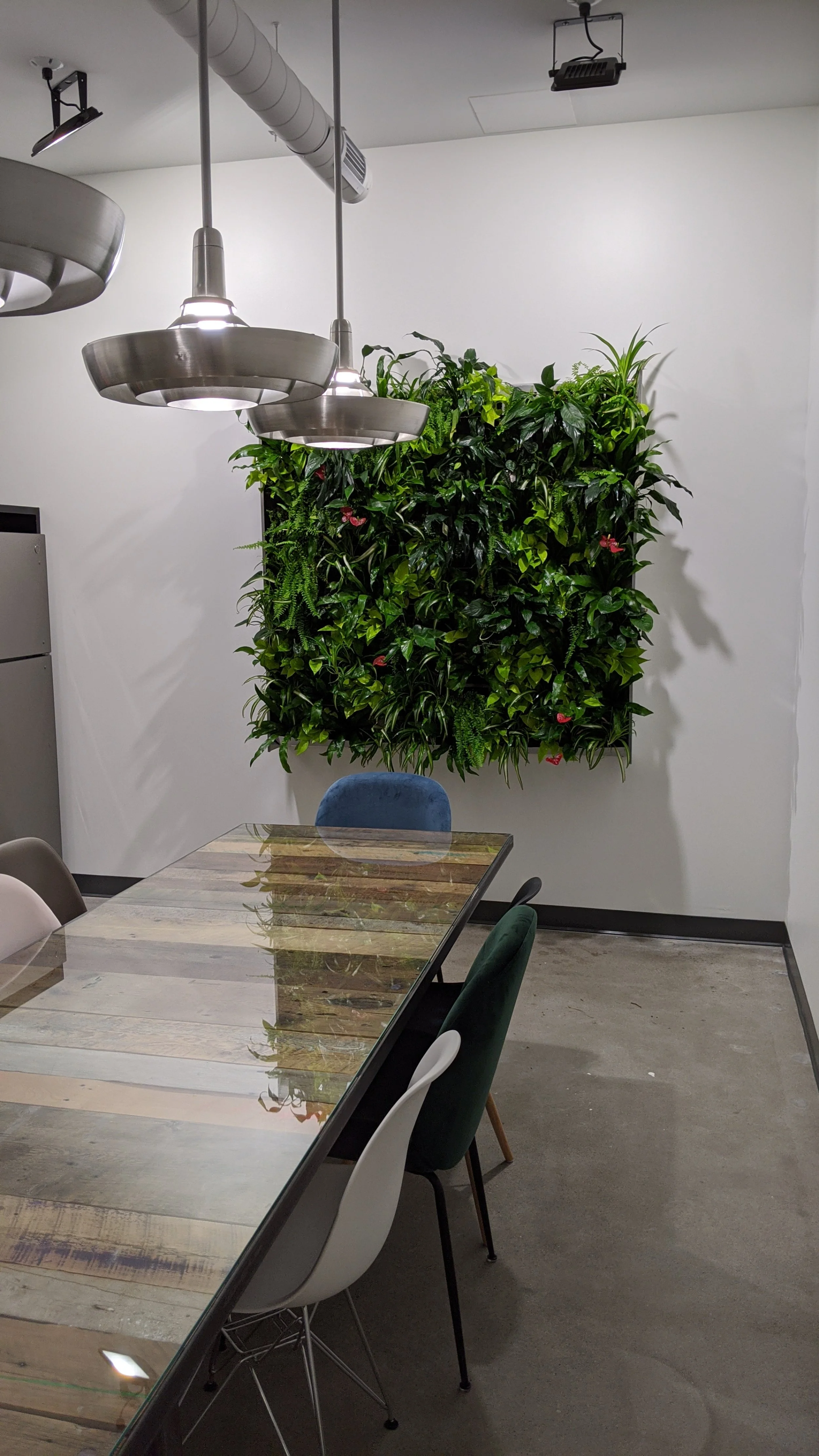 Salle de réunion avec un mur végétal, une table en bois, et plusieurs chaises.