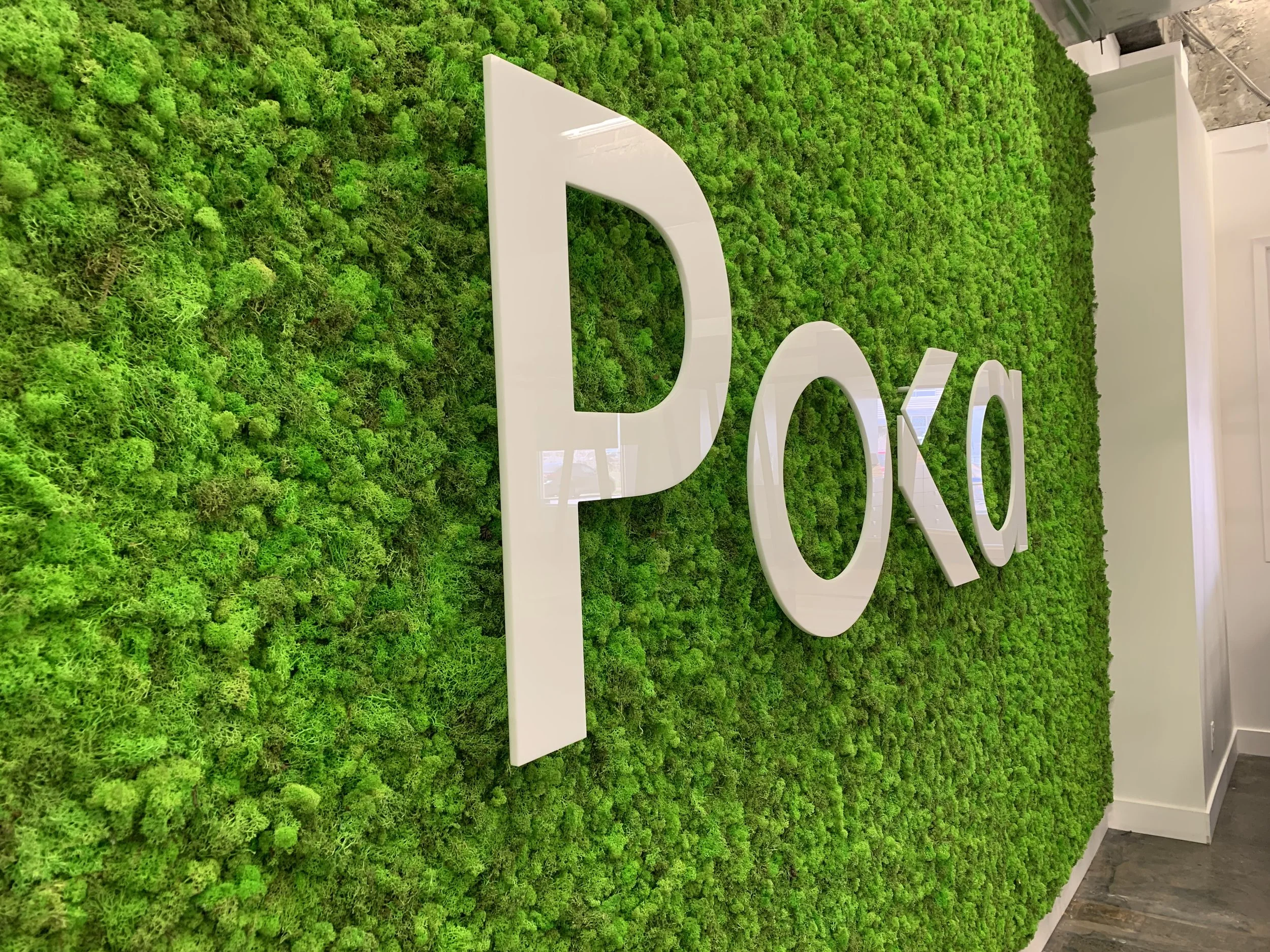 Mur recouvert de mousse verte avec lettres blanches formant le mot "POKA".