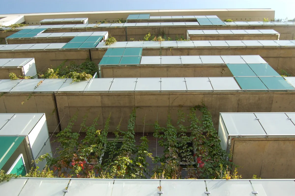 Vue d'un immeuble moderne avec des balcons recouverts de panneaux solaires et de la végétation en espalier sur le devant.