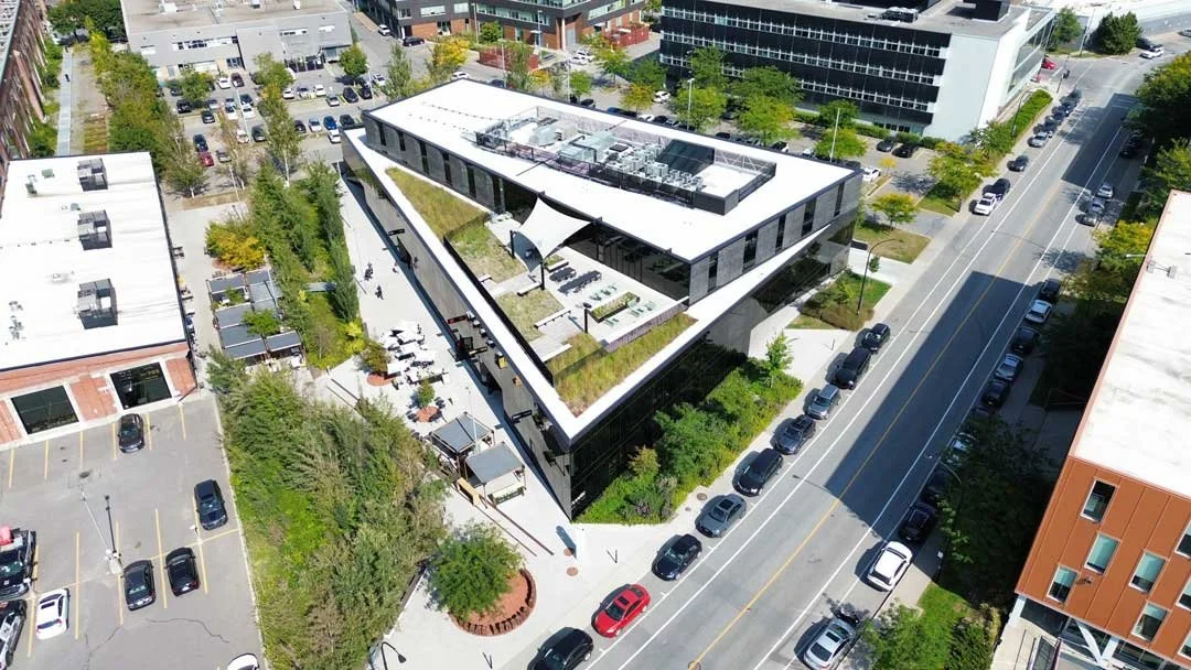 Vue aérienne d'un bâtiment moderne avec un toit végétalisé, entouré de rues et de places de parking.