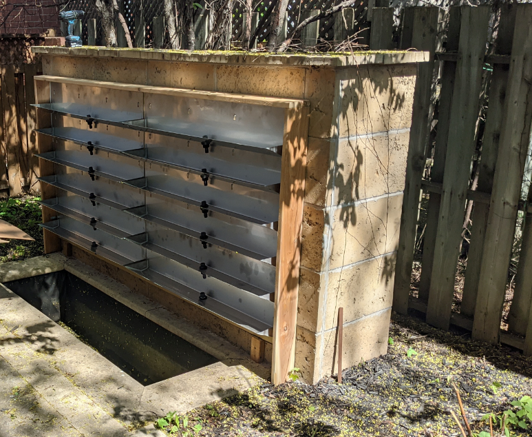 Un récupérateur d'eau en construction avec des étagères en métal et un mur en briques dans un jardin.