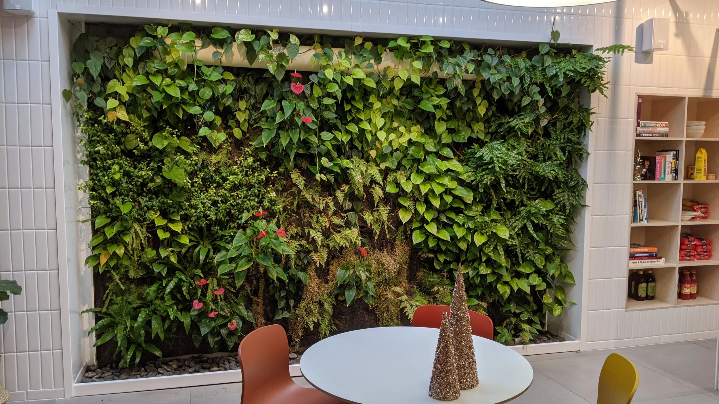 Murs végétaux avec diverses plantes vertes et fleurs dans une salle avec une table ronde, décorée de deux arbres en forme de cône.