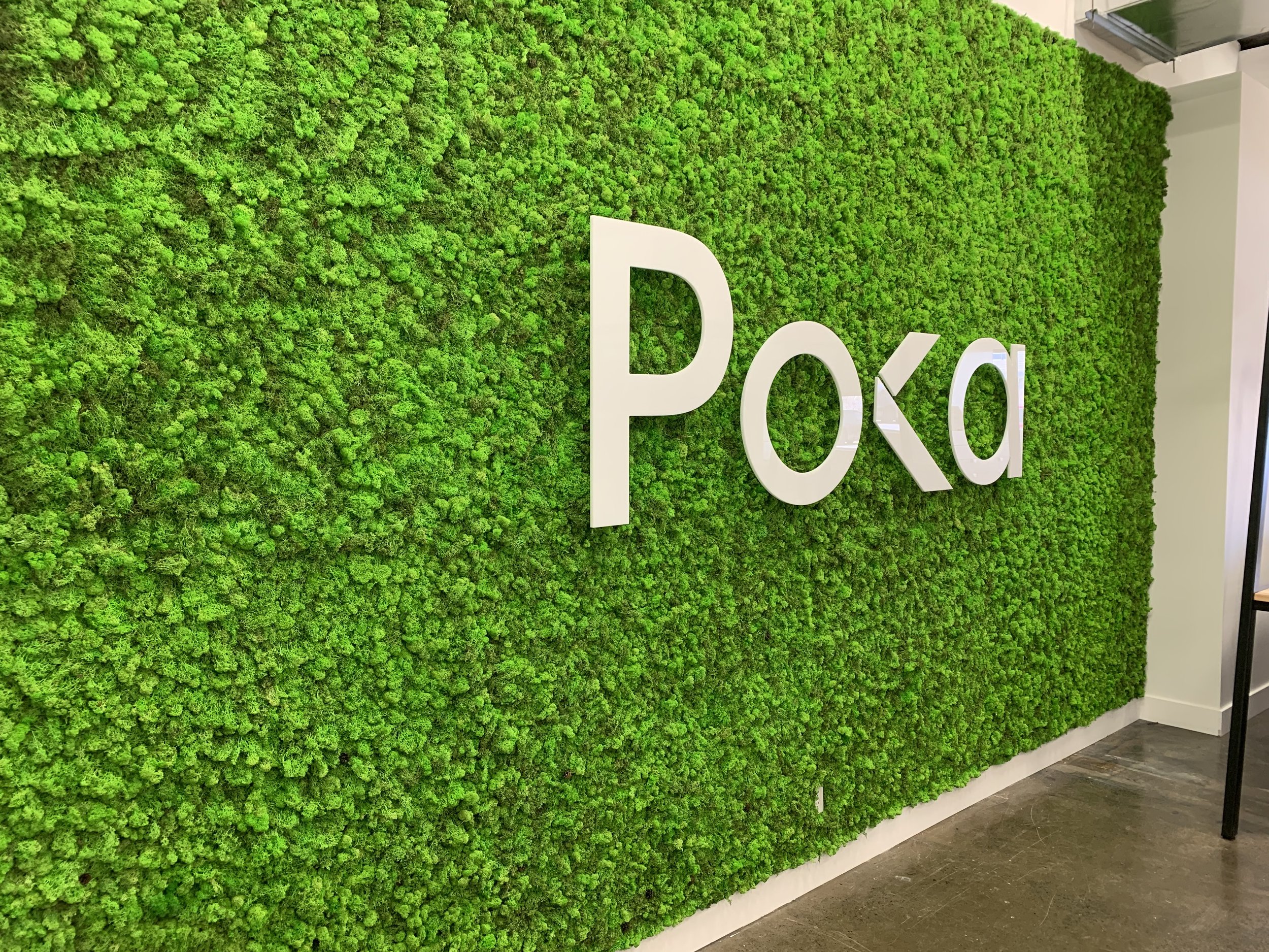 Mur végétal avec le logo blanc de Poka dans un espace intérieur.