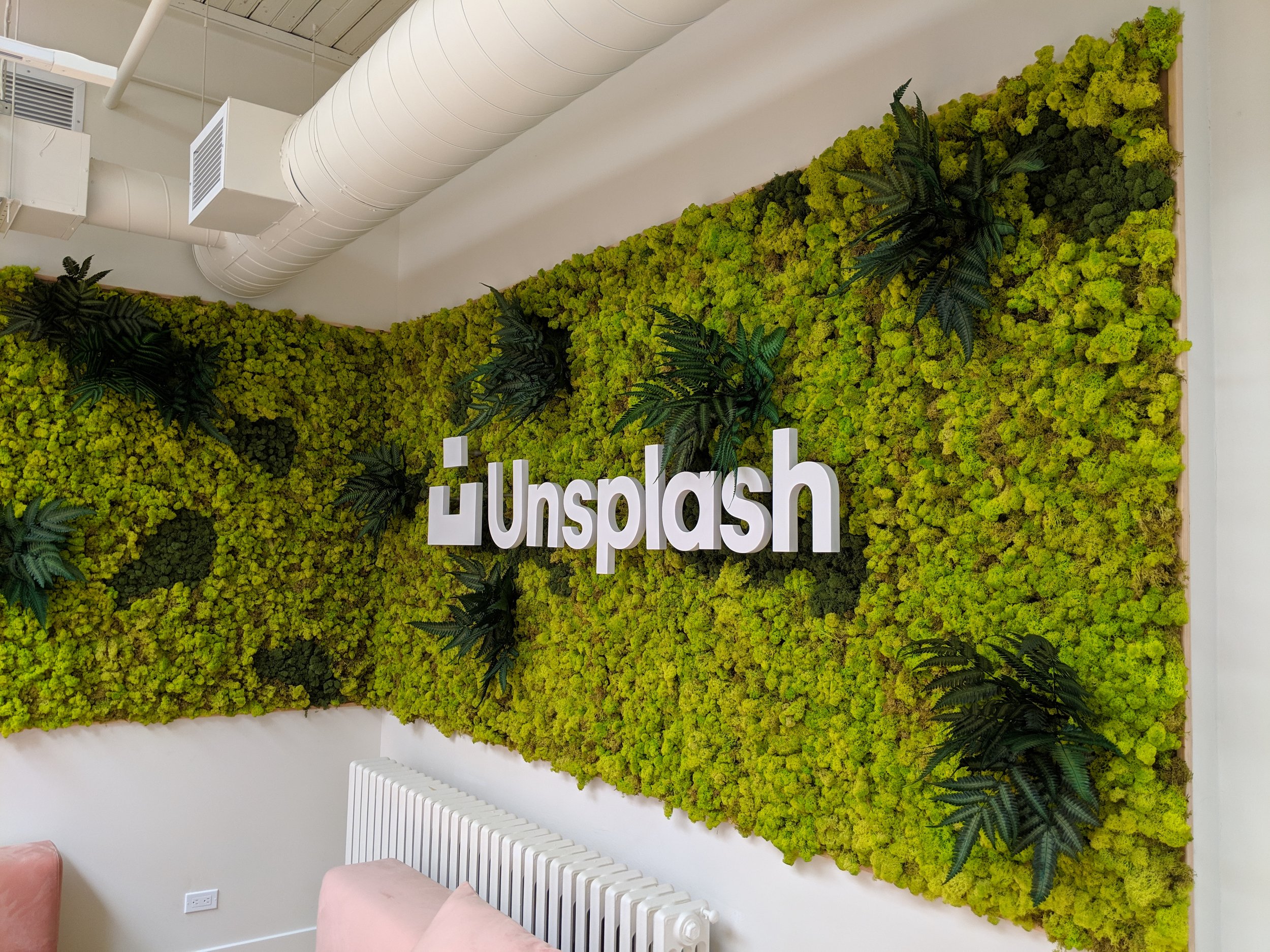 Murs végétaux verts avec le logo d'Unplash en lettres blanches en 3D.