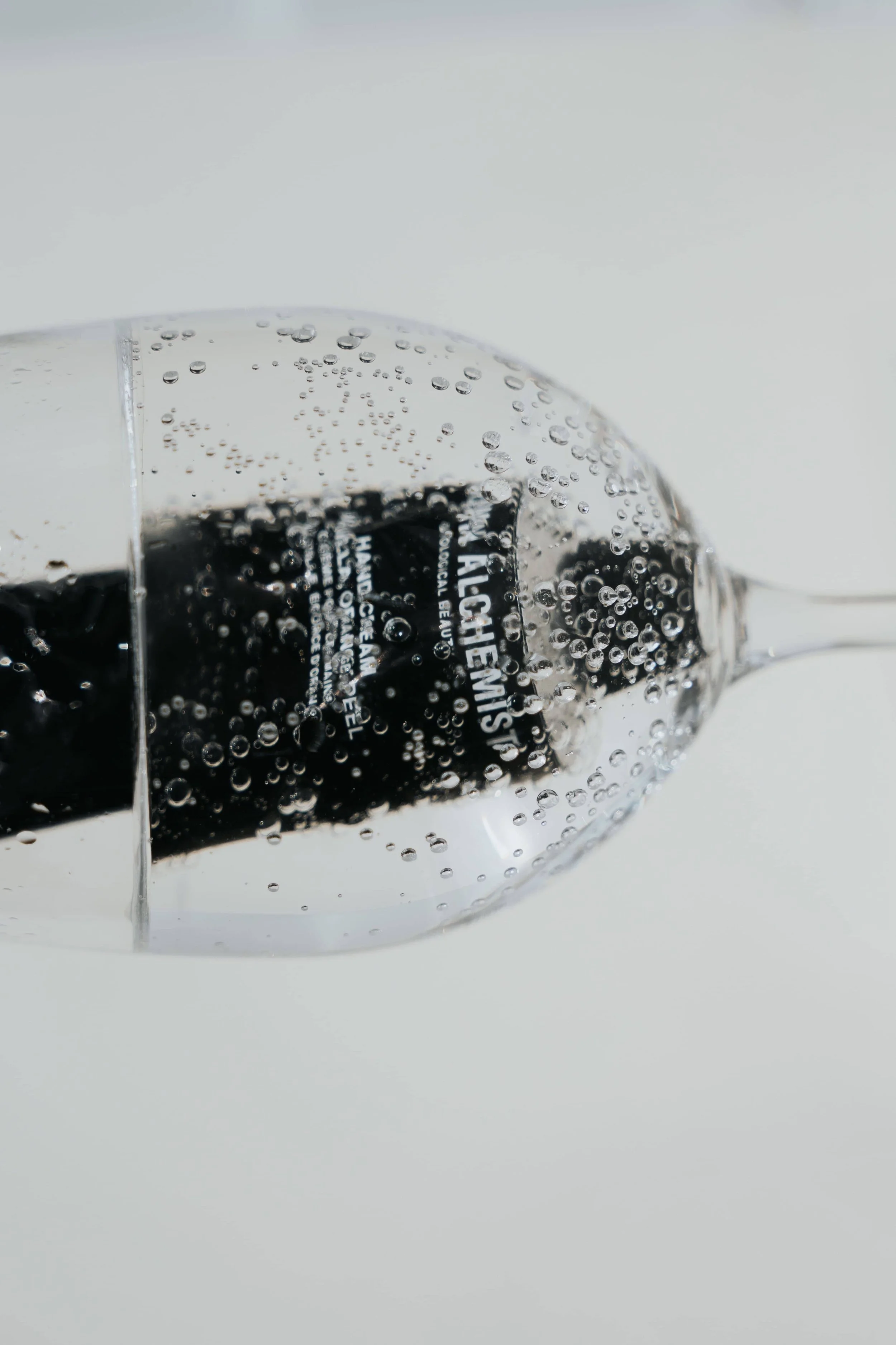 A close-up of a glass filled with a clear carbonated beverage, with bubbles rising inside, against a plain white background.
