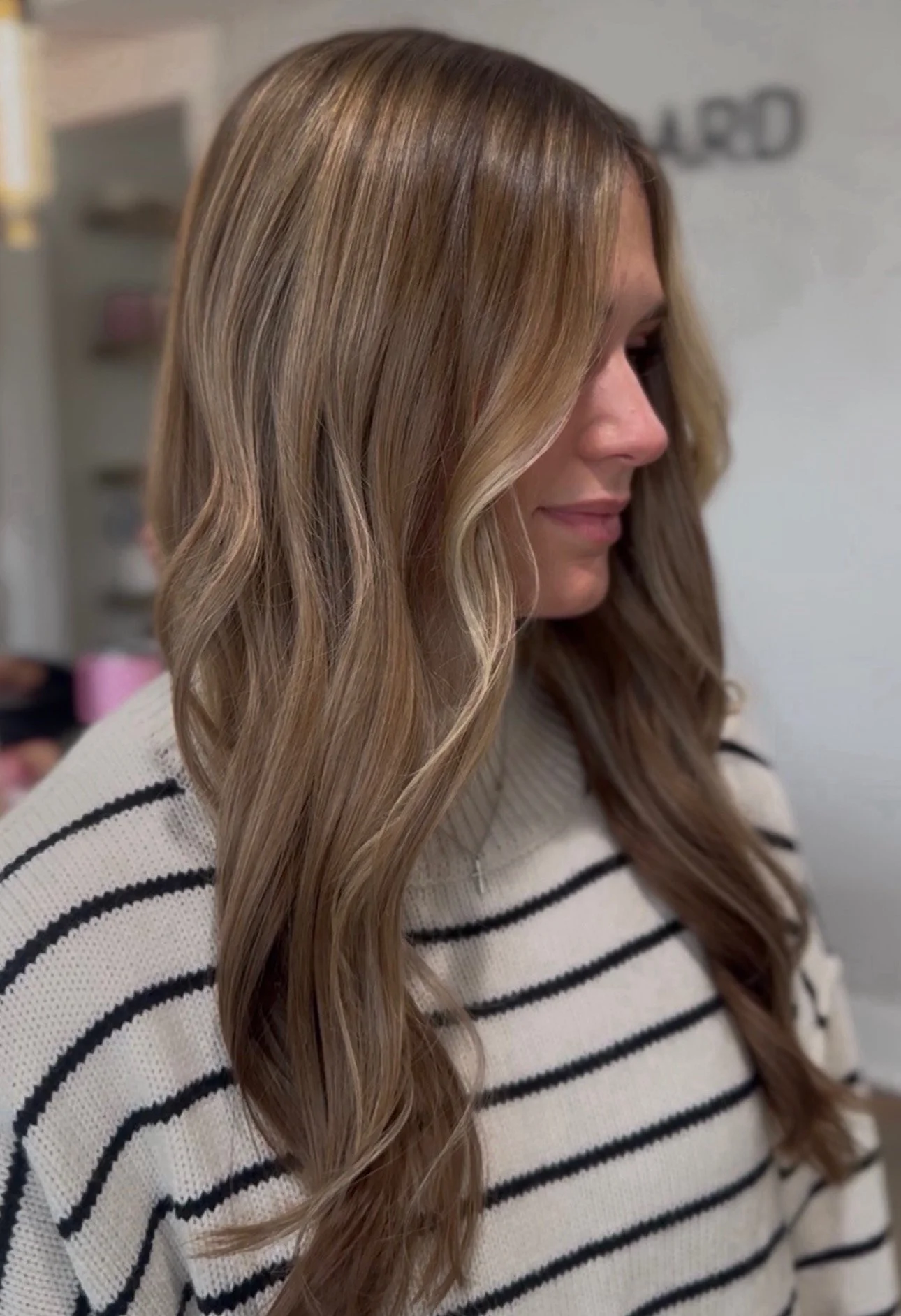 A woman with long, wavy, blonde hair wearing a white and black striped sweater, looking to her right.
