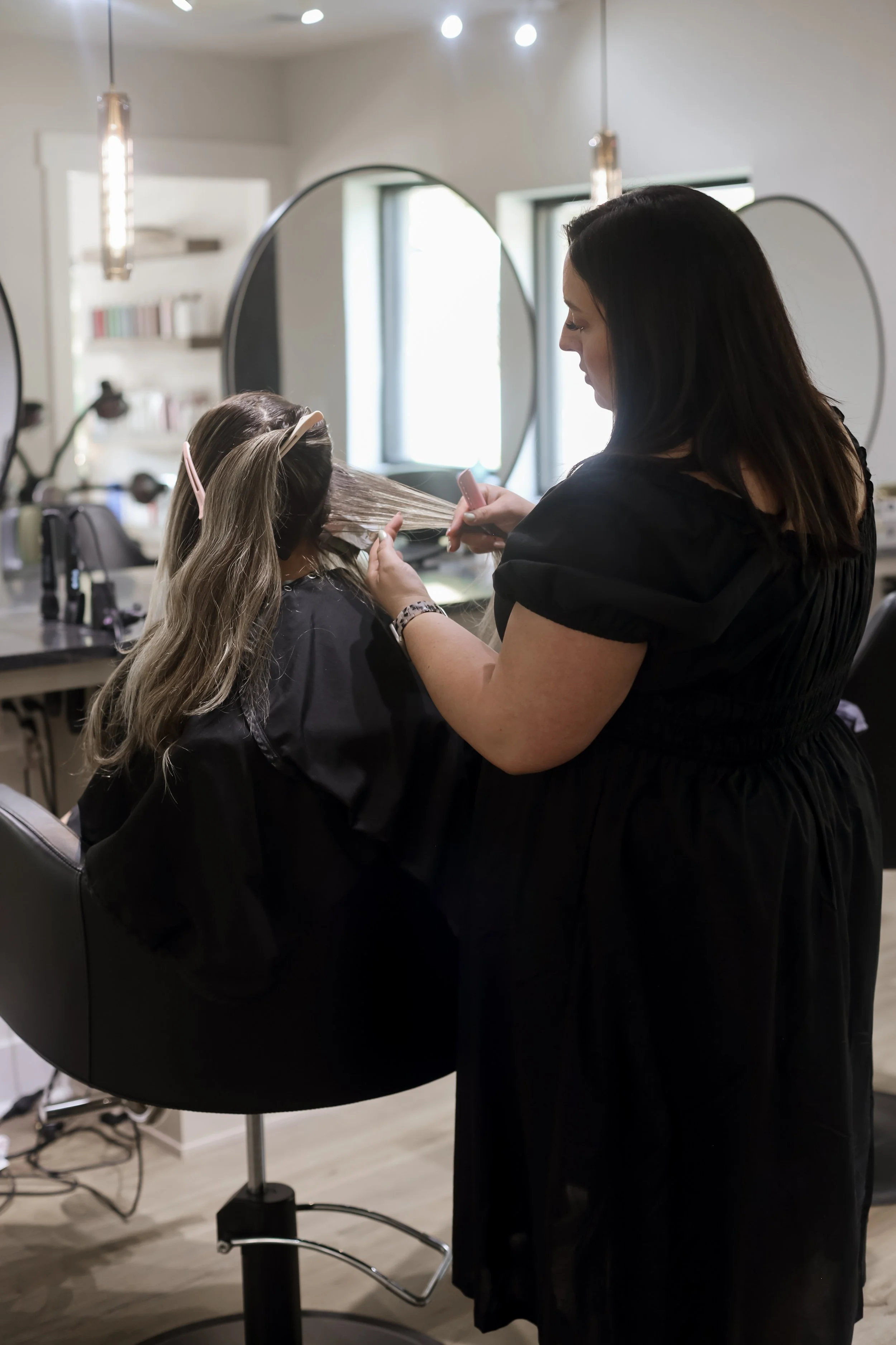 A hairstylist blow-drying a client's hair in a salon.