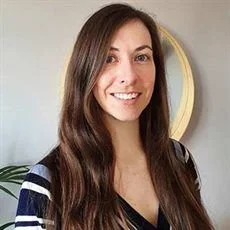 A woman with long brown hair smiling in front of a mirror.